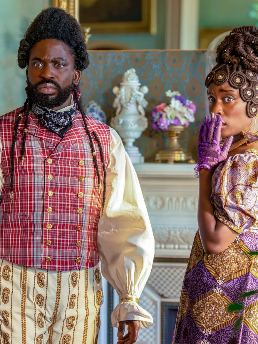 Actors Adjani Salmon and Babirye Bukilwa stand together dressed in Regency-era clothing, in a still from "Dreaming Whilst Black." 