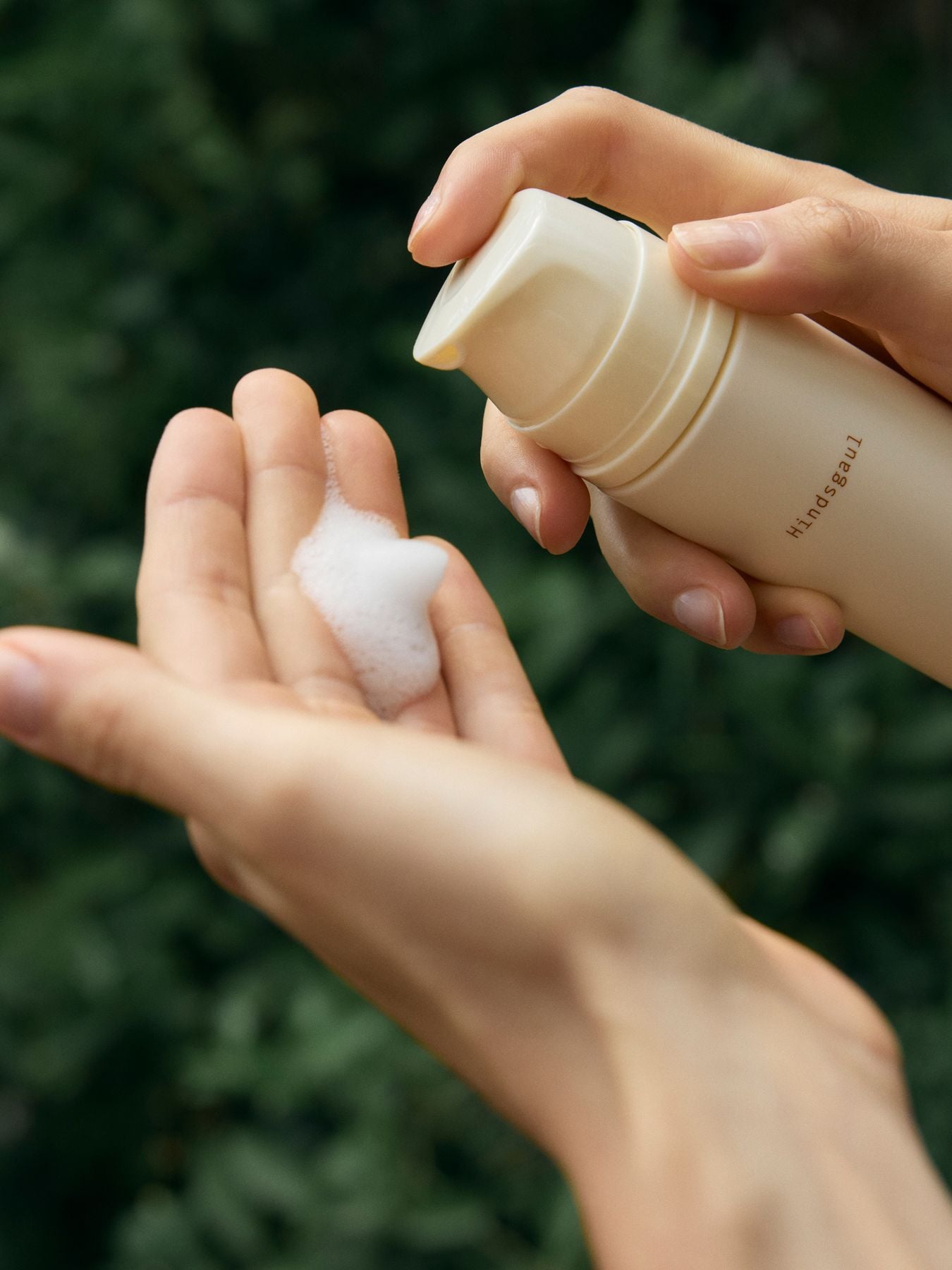 A model's hands holds a bottle of the Hindsgaul Hair mousse and pumps it into their hands 