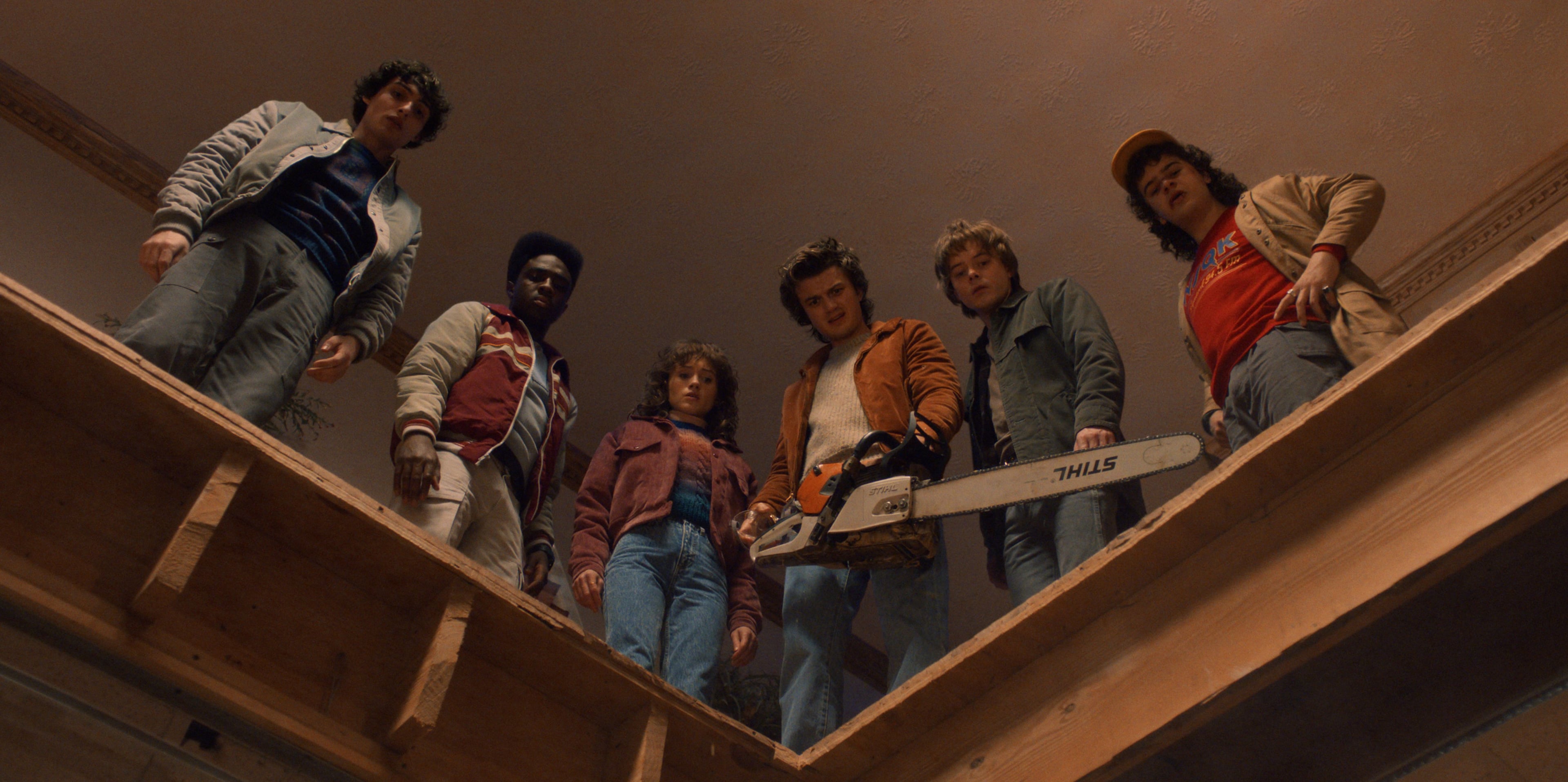 The cast of Stranger Things stand looking down at a hole they just cut into the floor, in a scene from season five. 