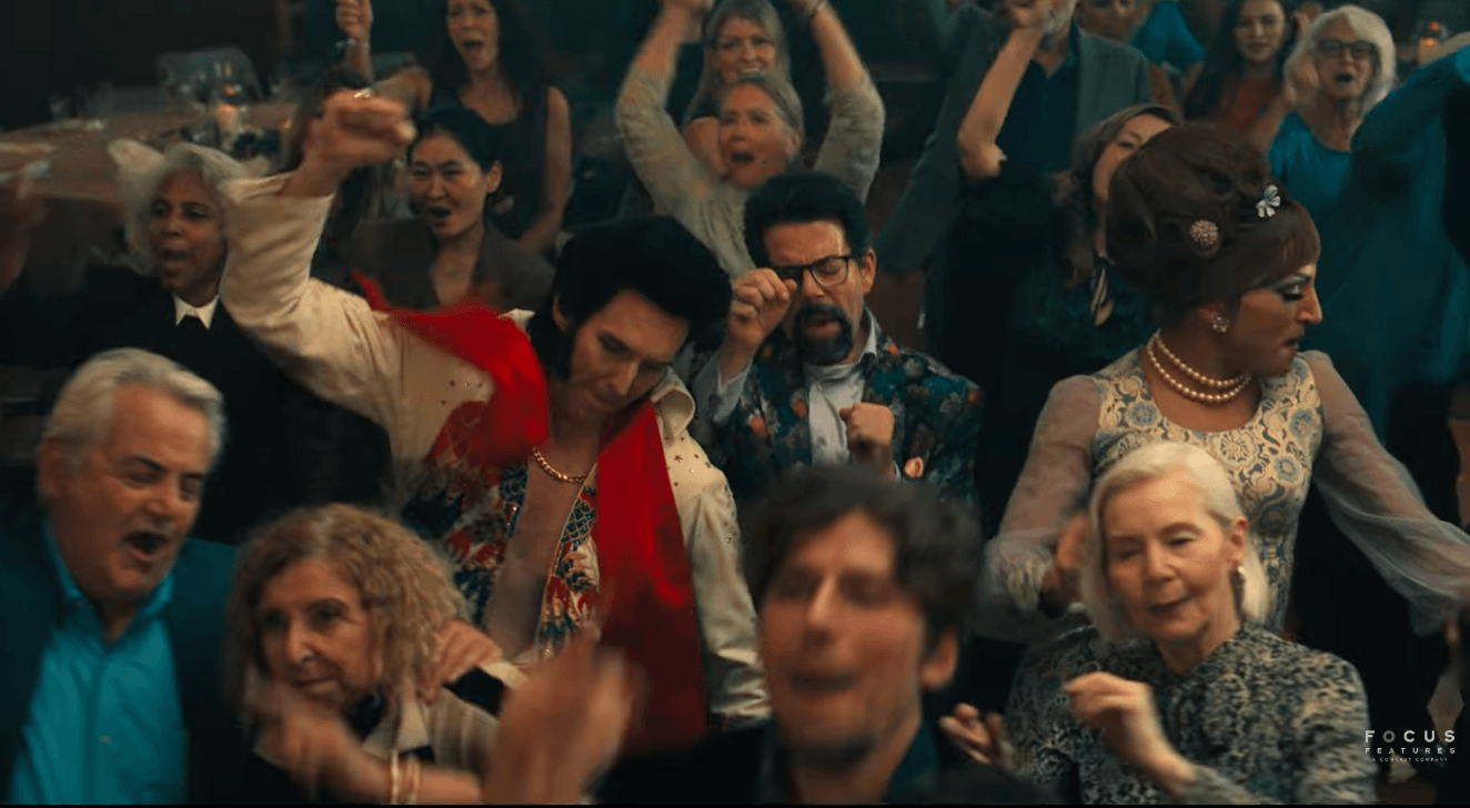 Weddings guests, some dressed as music impersonators, dance in a crowd in a still from 'Song Sung Blue." 