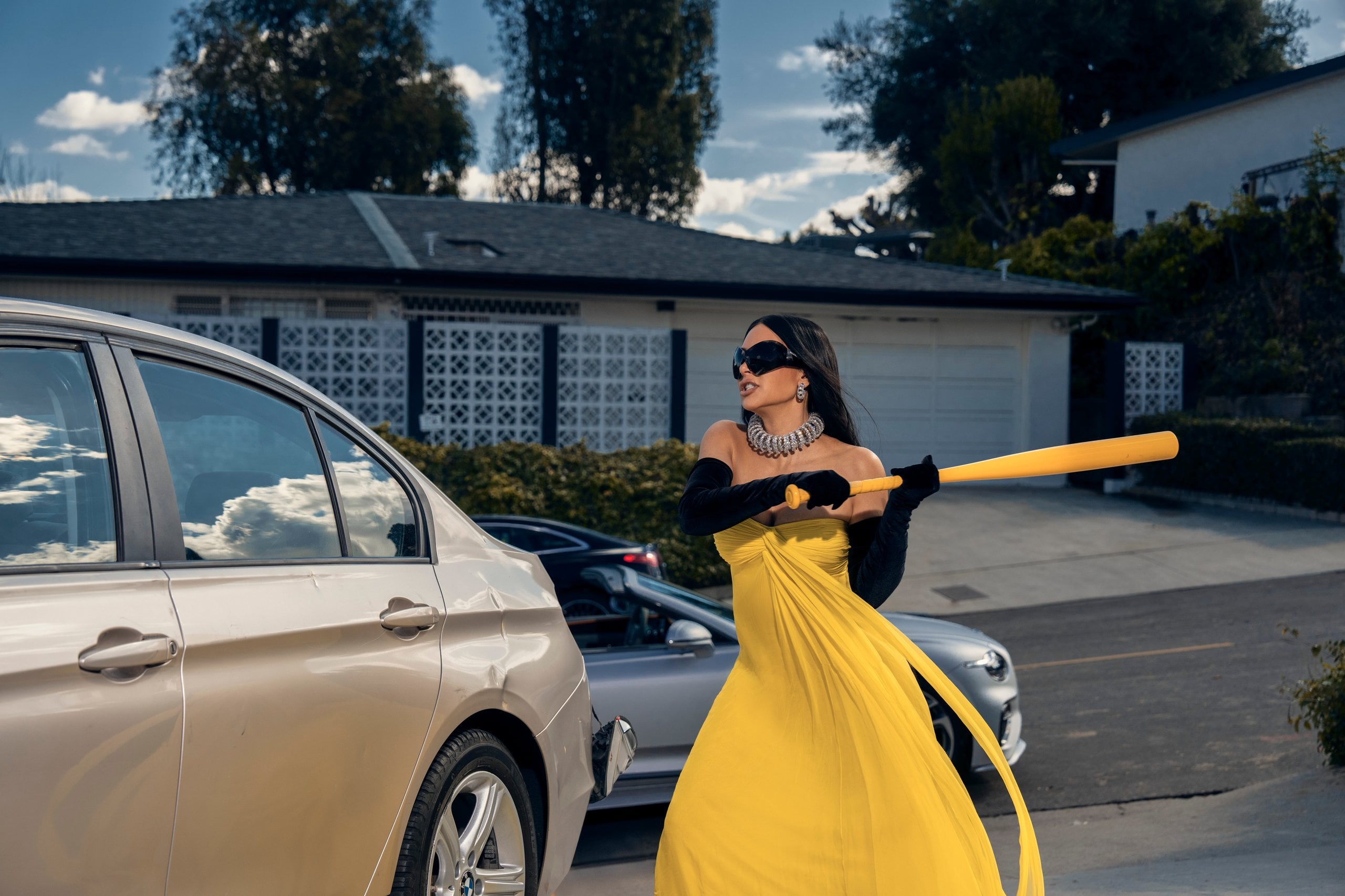 Kim Kardashian takes a baseball bat to a car, wearing a yellow gown, in a still from All's Fair.
