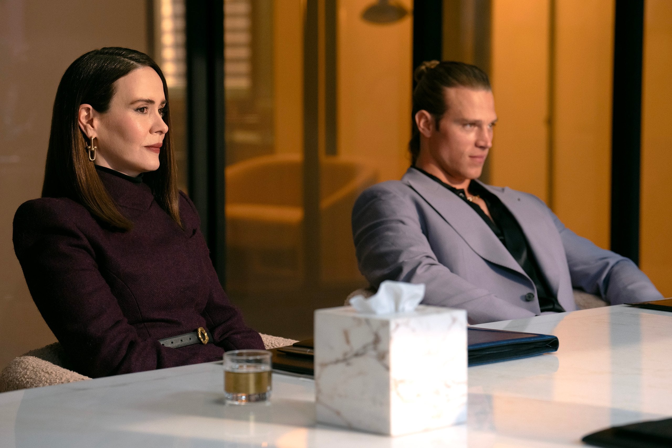 Actors Sarah Paulson and Matthew Noszka sit at an office table in a still from All's Fair.