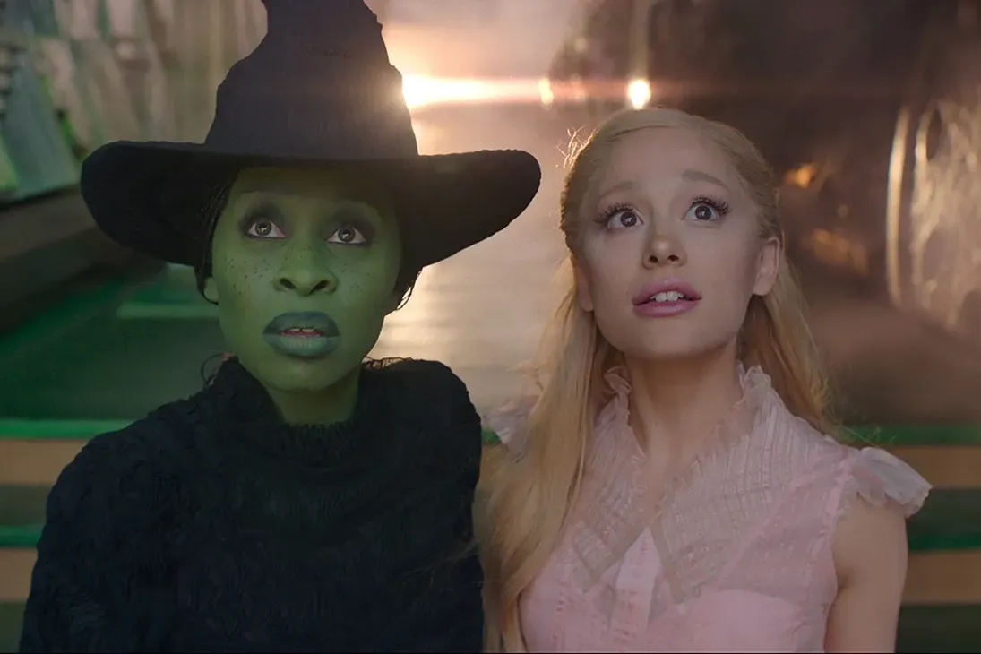 Cynthia Erivo as Elphaba, with green skin and a black witch-like ensemble, and Ariana Grande, as Glinda, dressed in a pink frilly dress, in a still from "Wicked."