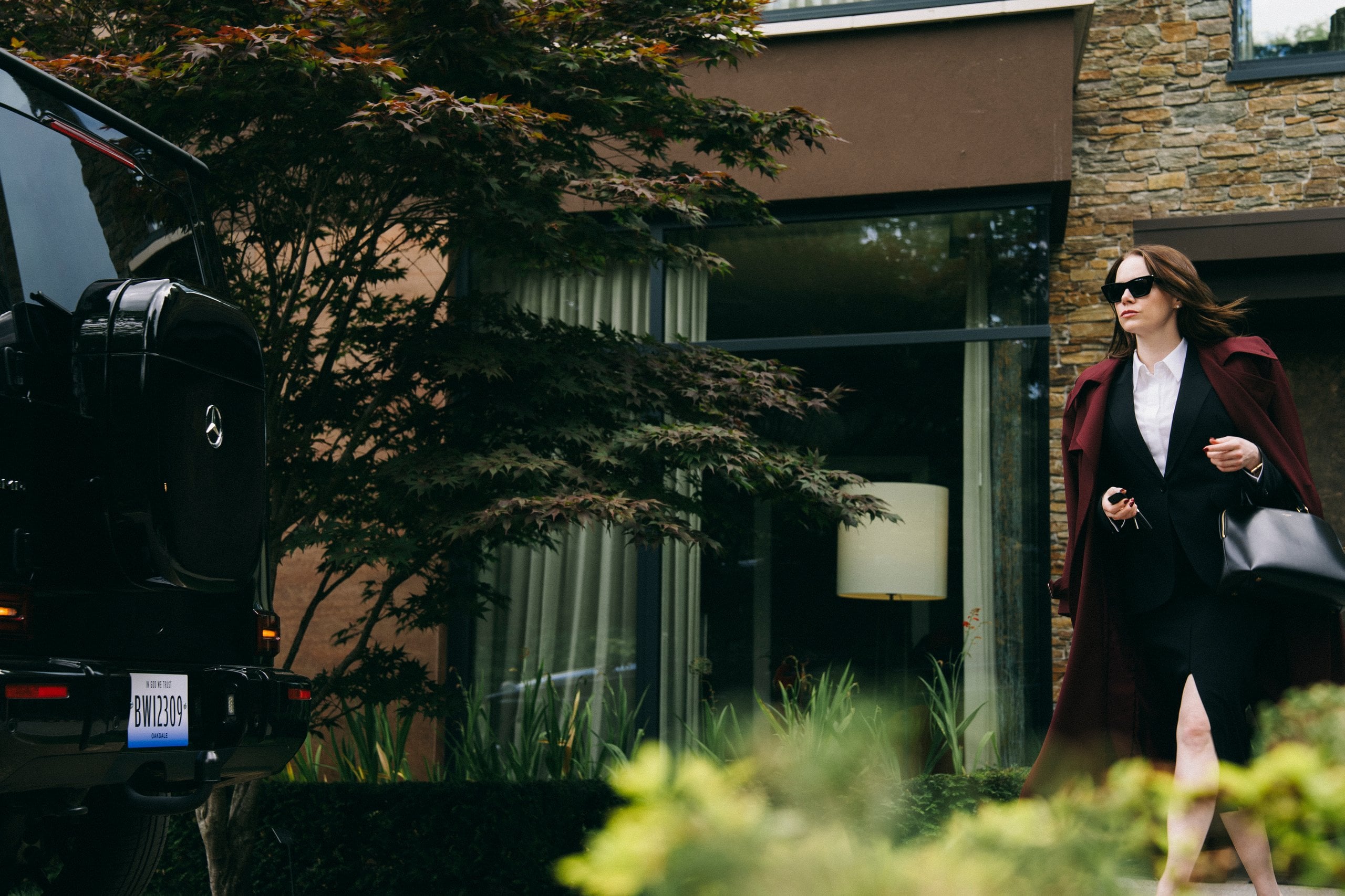 Emma Stone exits a fancy house on her way to her car in a still from "Bugonia."