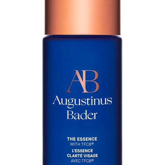 A bottle of Augustinus Bader The Essence, a blue bottle with a gold cap, against a white background