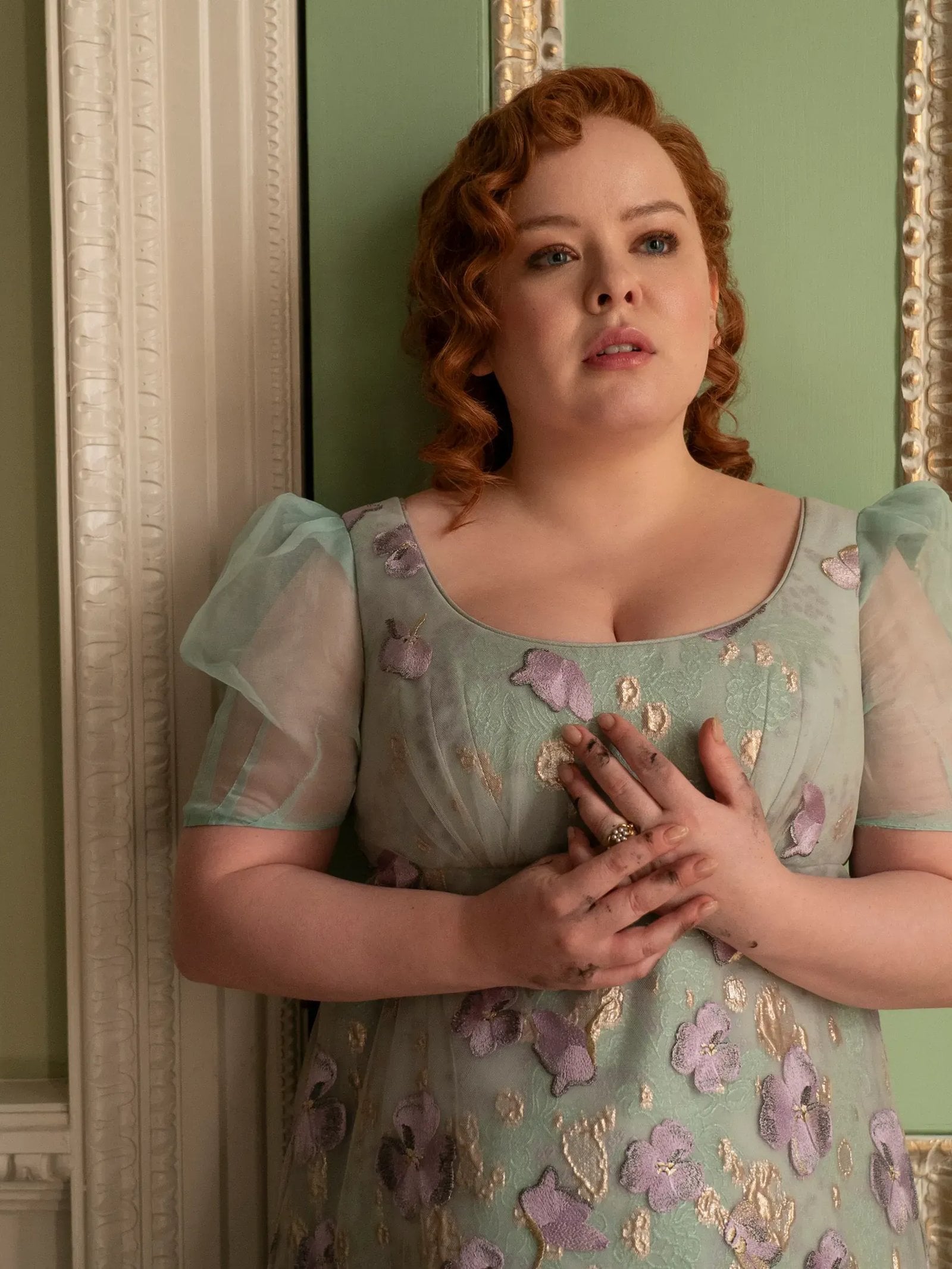 Actress Nicola Coughlan wears a seafoam-green dress and stands agains a green-and-gold wall in a scene from Bridgerton.