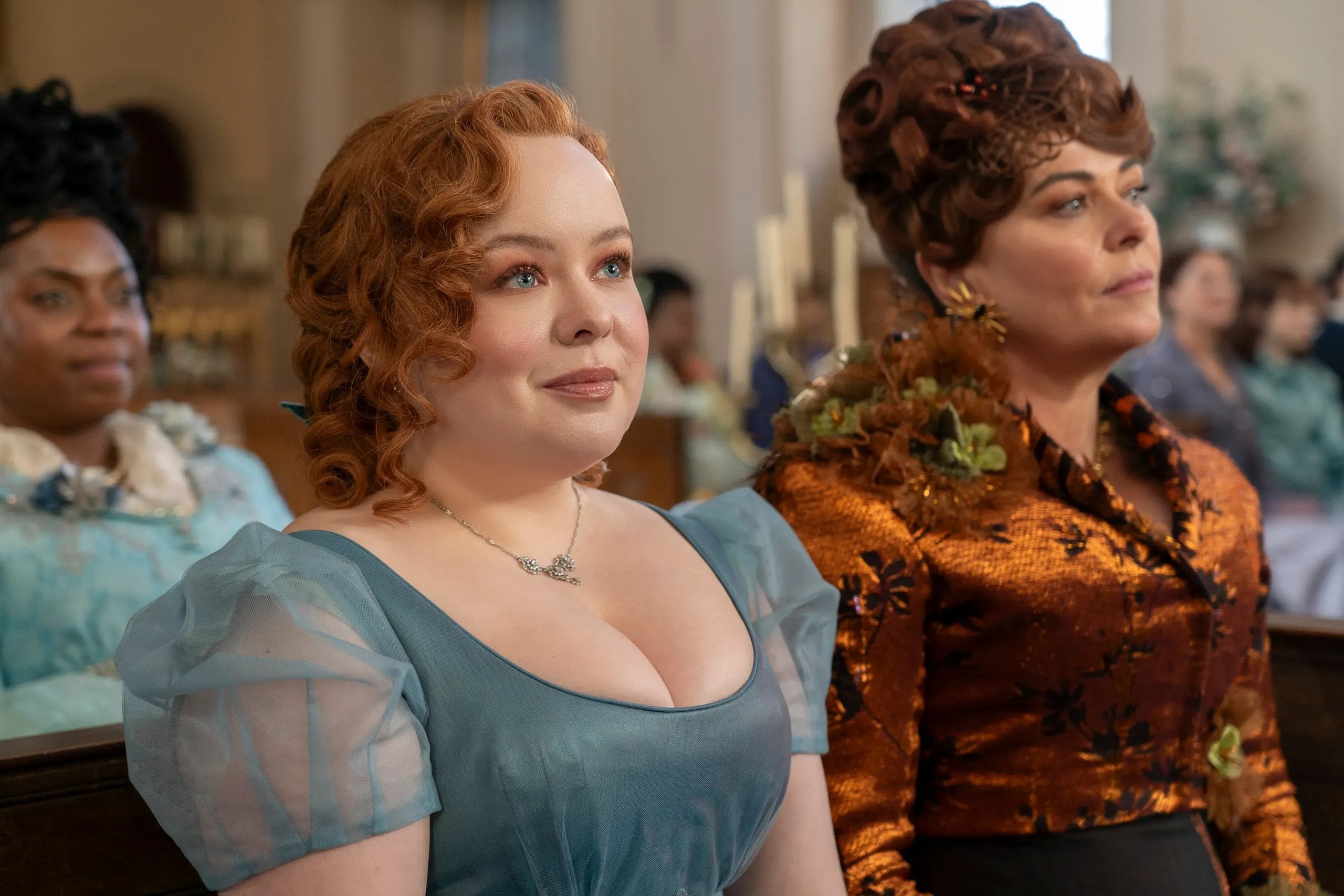 Actress Nicola Coughlan sits next to her mother, played by Polly Walker, from a scene in Bridgerton, wearing a blue dress with sheer puffy sleeves.