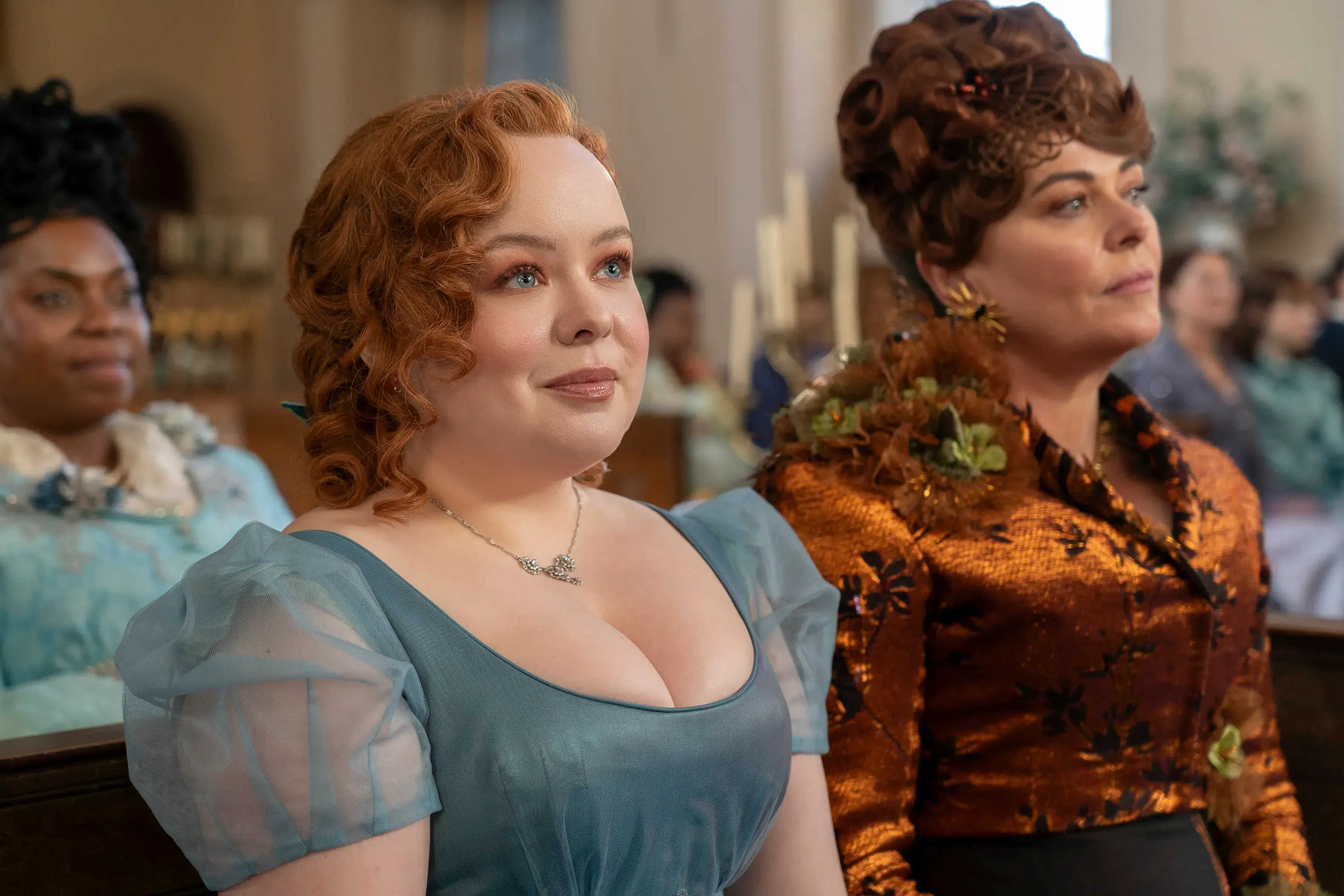 Actress Nicola Coughlan sits next to her mother, played by Polly Walker, from a scene in Bridgerton, wearing a blue dress with sheer puffy sleeves.