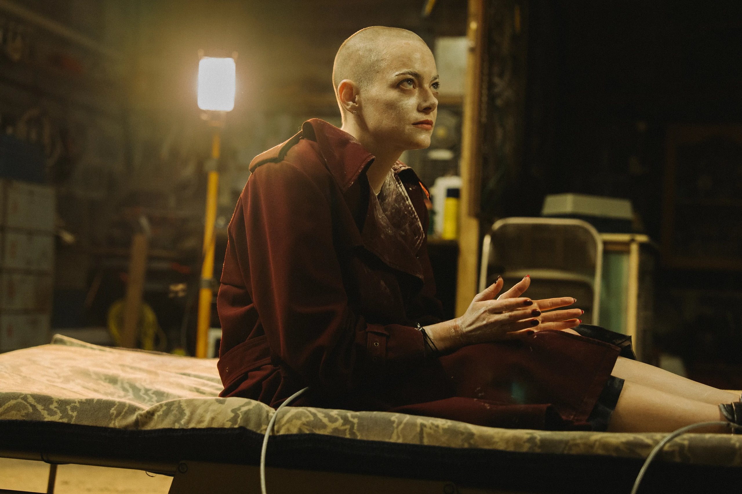 Actor Emma Stone sits on a cot with her head shaved and covered in white dust in a still from "Bugonia."