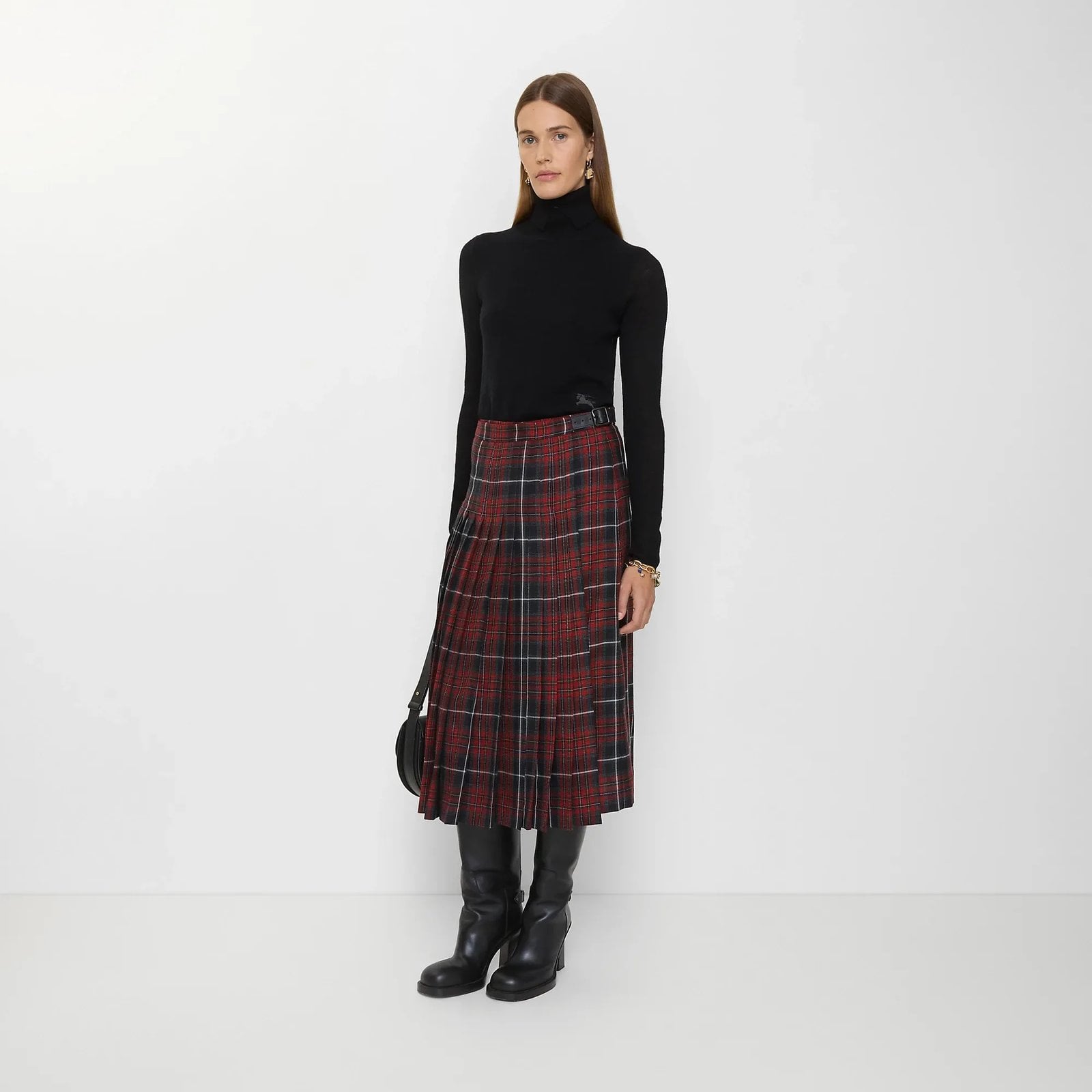 A model wears the Burberry Check Wool Blend Midi Kilt with a black turtleneck and black boots.