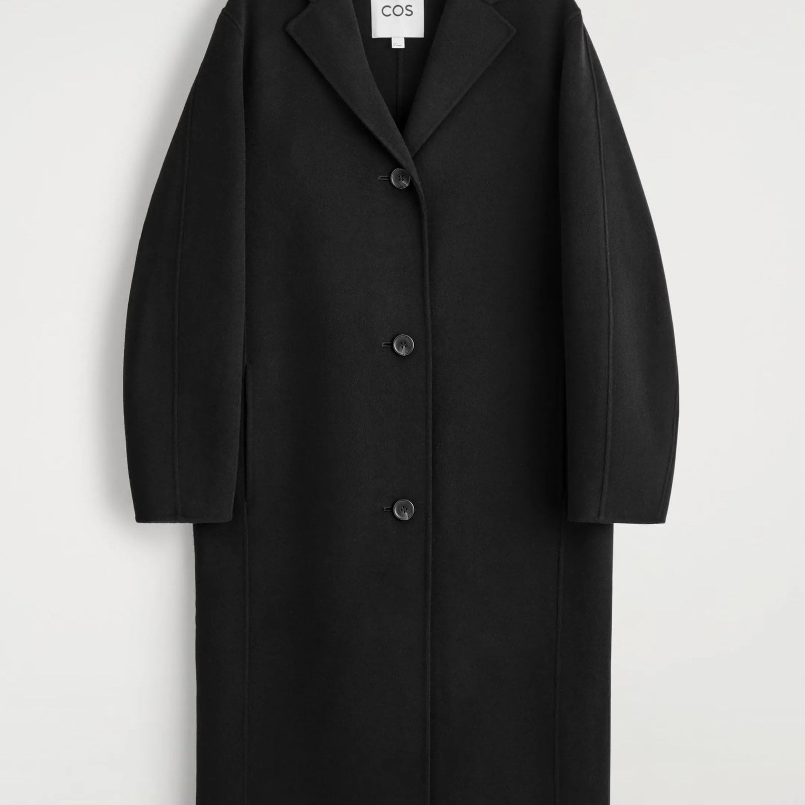 A COS black cocoon-shaped wool coat against a gray background