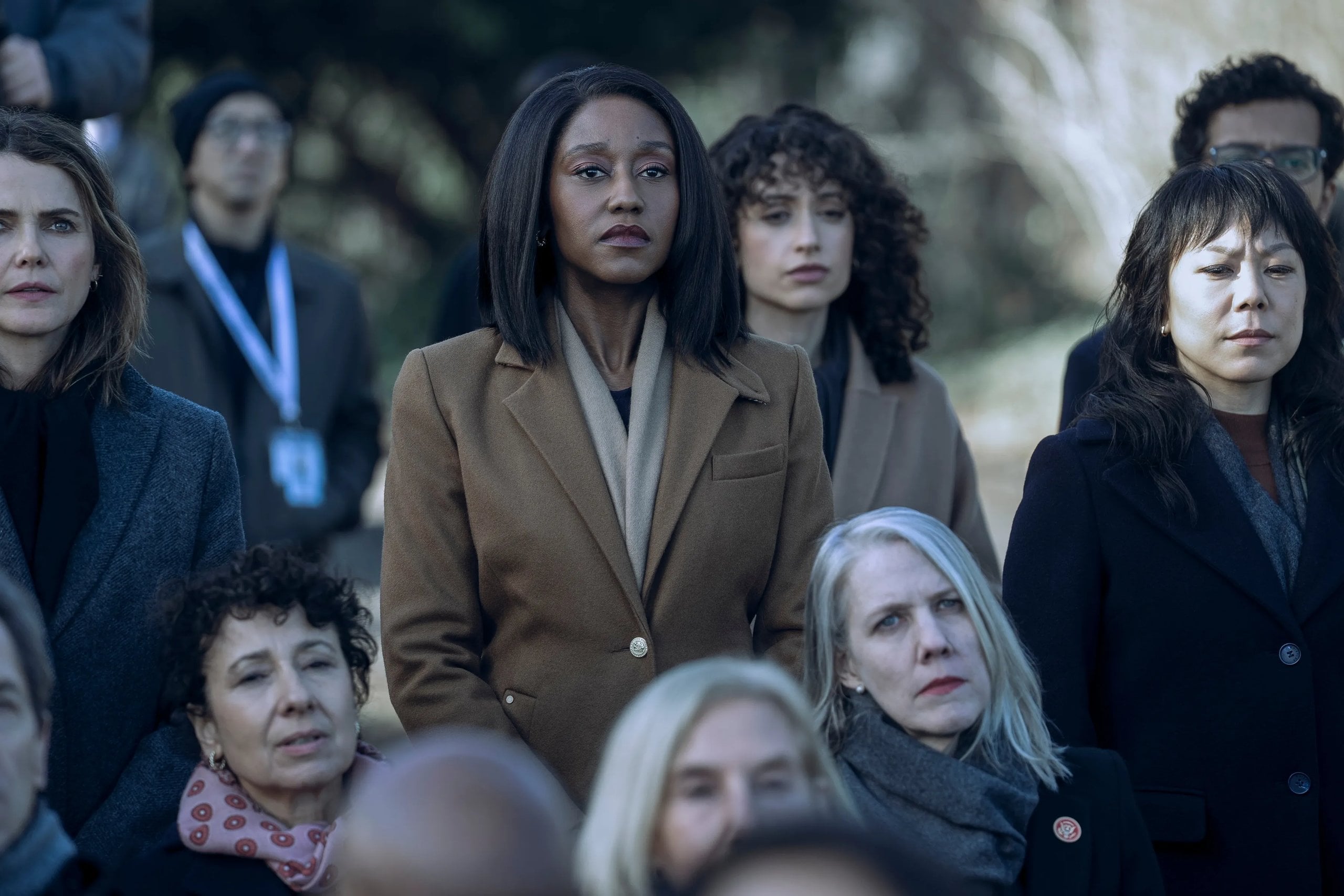 Nana Mensah stands in a crowd looking onward in a still from The Diplomat.