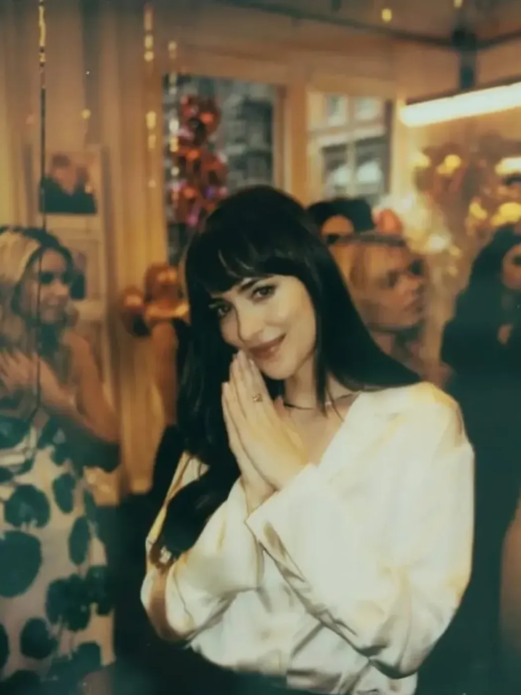 Dakota Johnson stands in front of a crowd in a white silk shirt.