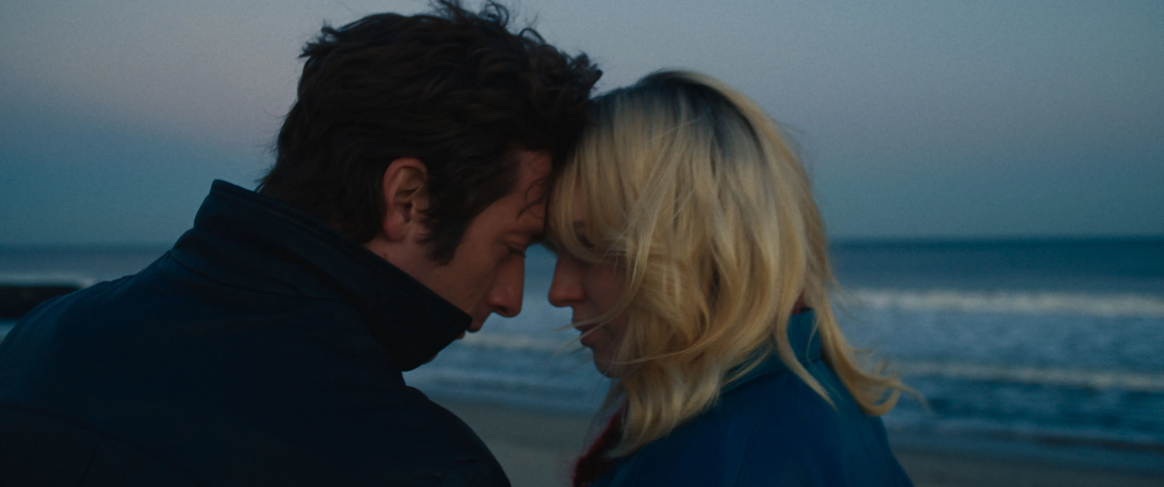 Actors Jeremy Allen White and Odessa Young lean in towards each other on a beach in a still from "Deliver Me From Nowhere."