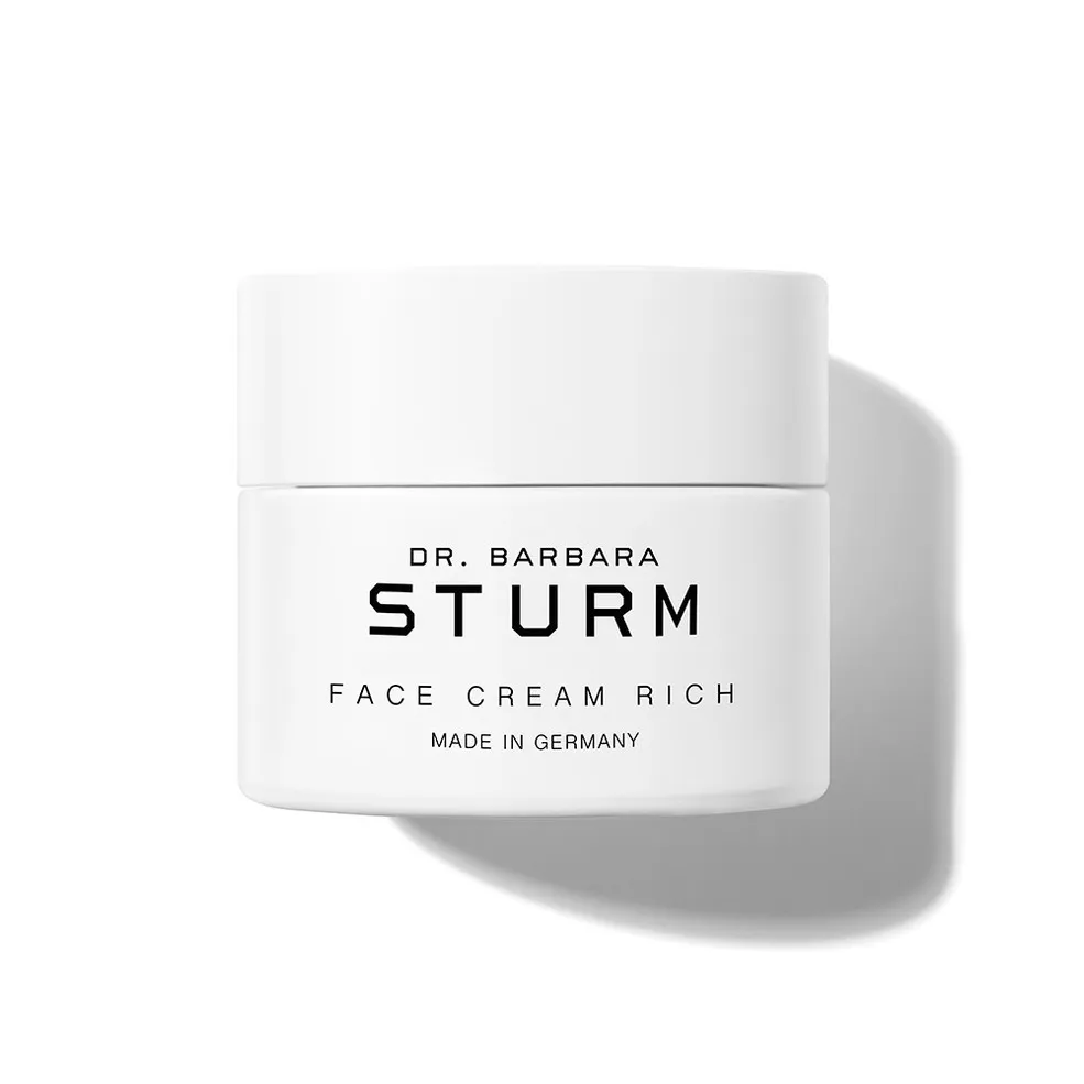 A white jar of face cream with black lettering against a white background, the label says Dr. Barbara Sturm Face Cream Rich
