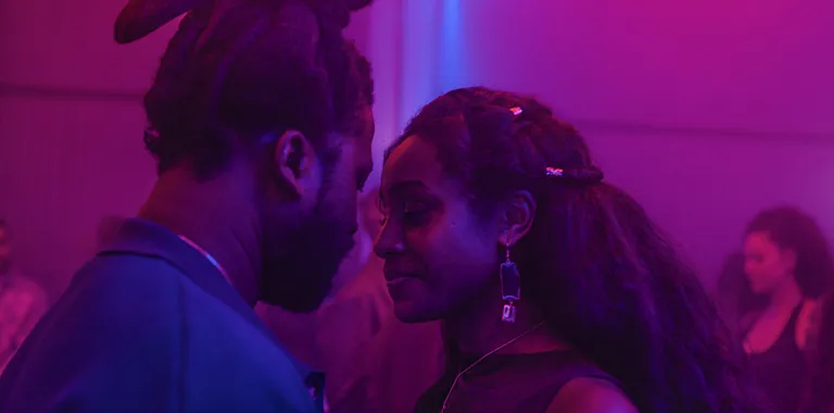 Bathed in purple lights, actors Adjani Salmon and Adjoa dance closely in a still from "Dreaming Whilst Black."