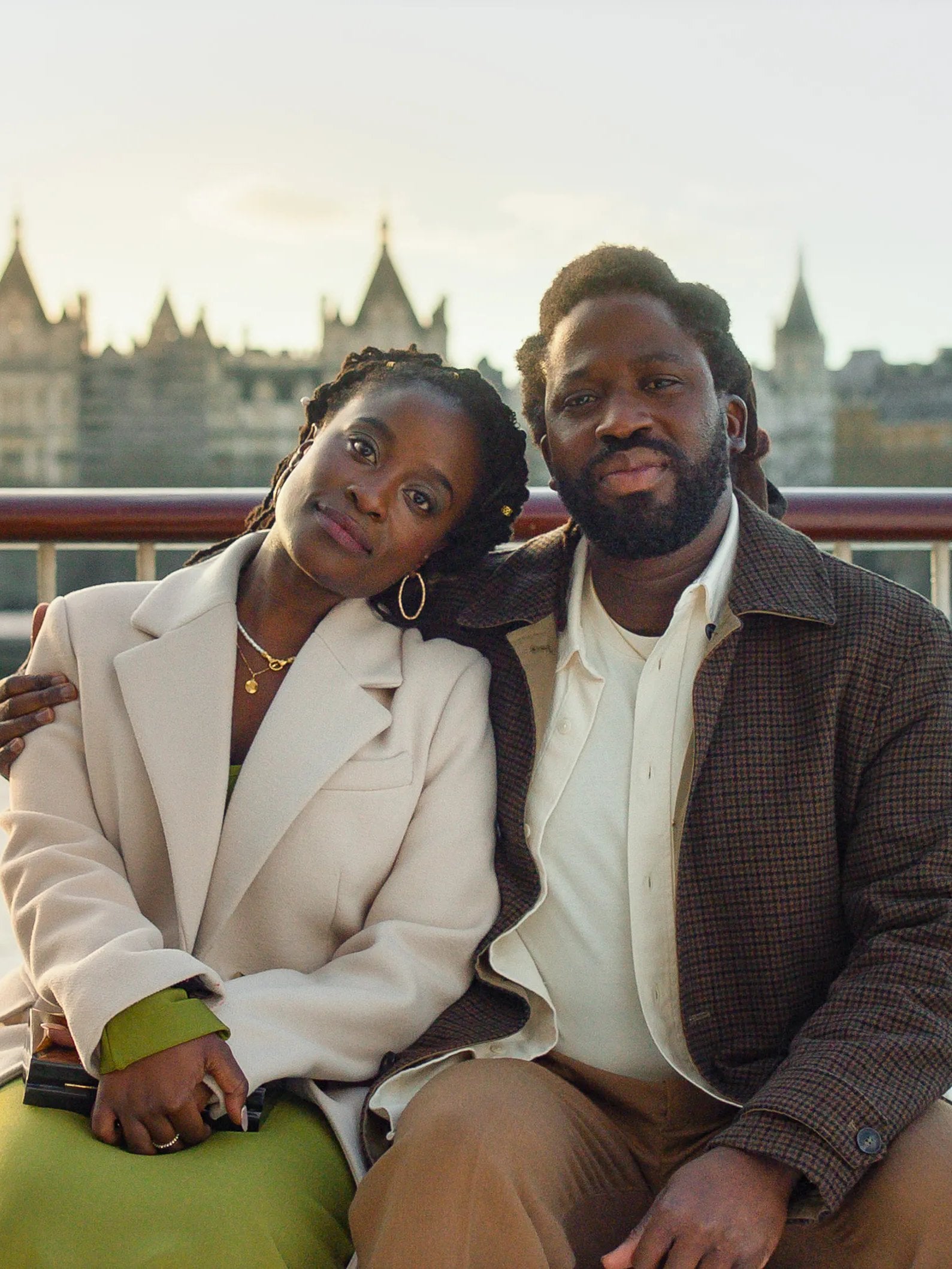 Actors Adjani Salmon and Babirye Bukilwa sit on a bench in front of the Thames River in a still from "Dreaming Whilst Black."