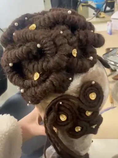 A mannequin head covered in rolled locs arranged in a Regency Era-style updo.