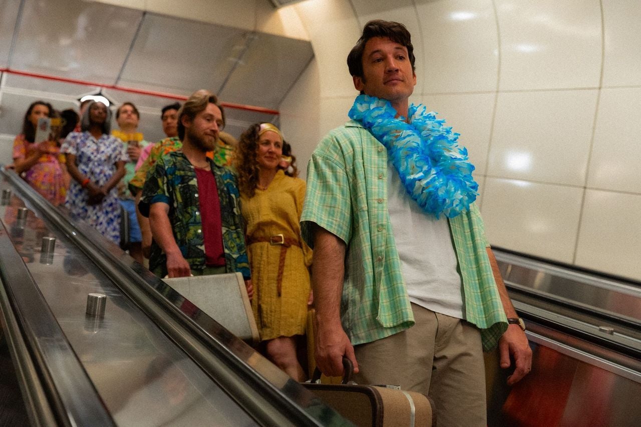 Actor Miles Teller stands on an escalator in a Hawaiian shirt and lei.