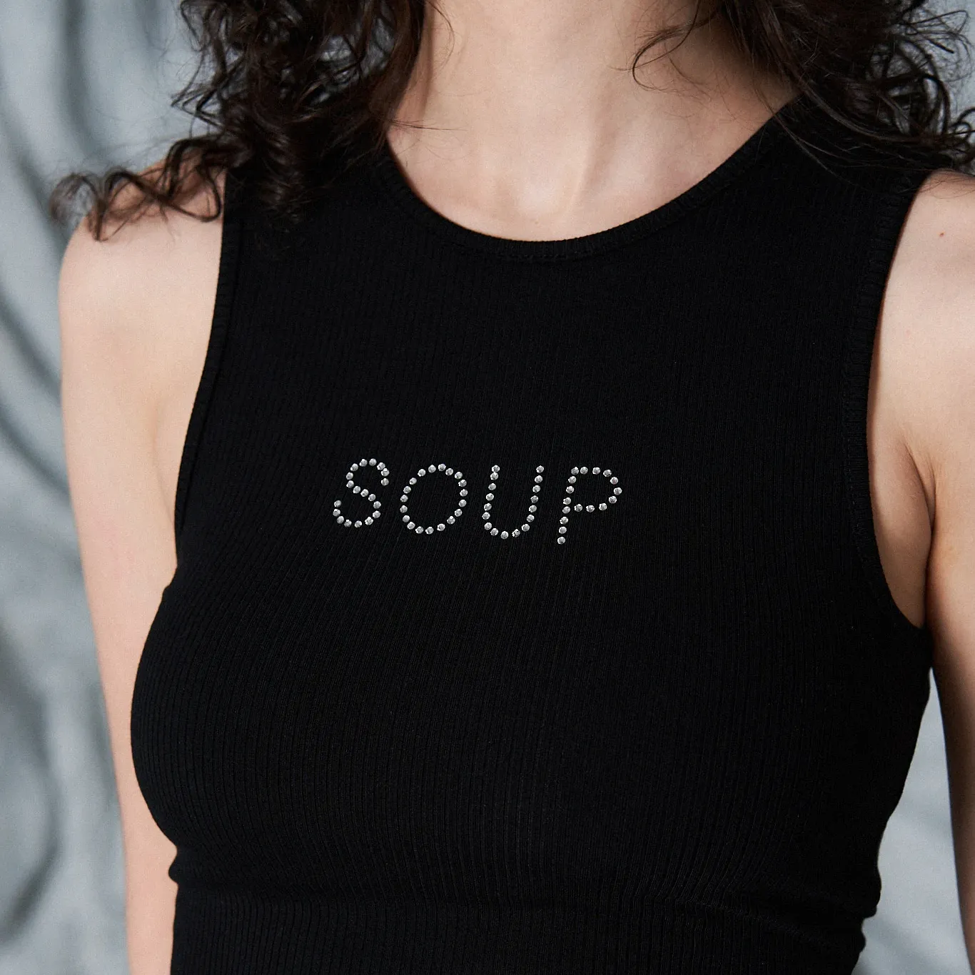 The torso of a model wearing a black tank top that says SOUP on it in crystals