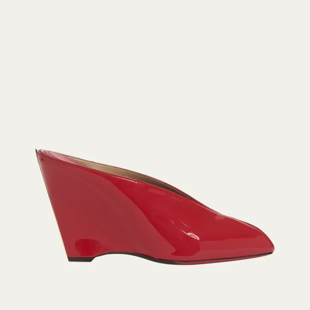 The Ferragamo Alicia Patent Leather Peep-Toe Wedge Mules in a bright red color against a cream background