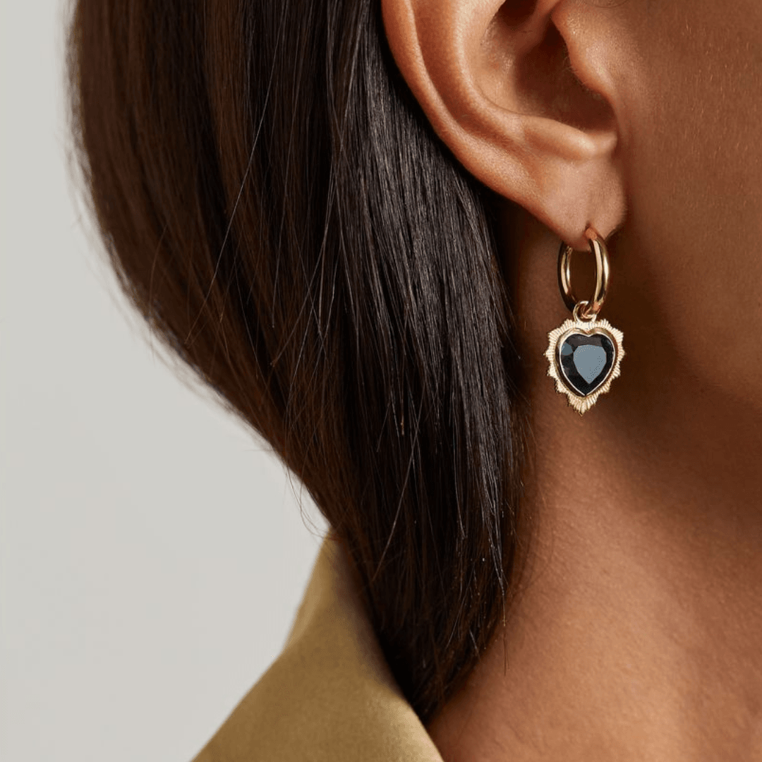 A close-up of a model's ear wearing the Foundrae Gemstone Heart 18-karat gold topaz single hoop earring