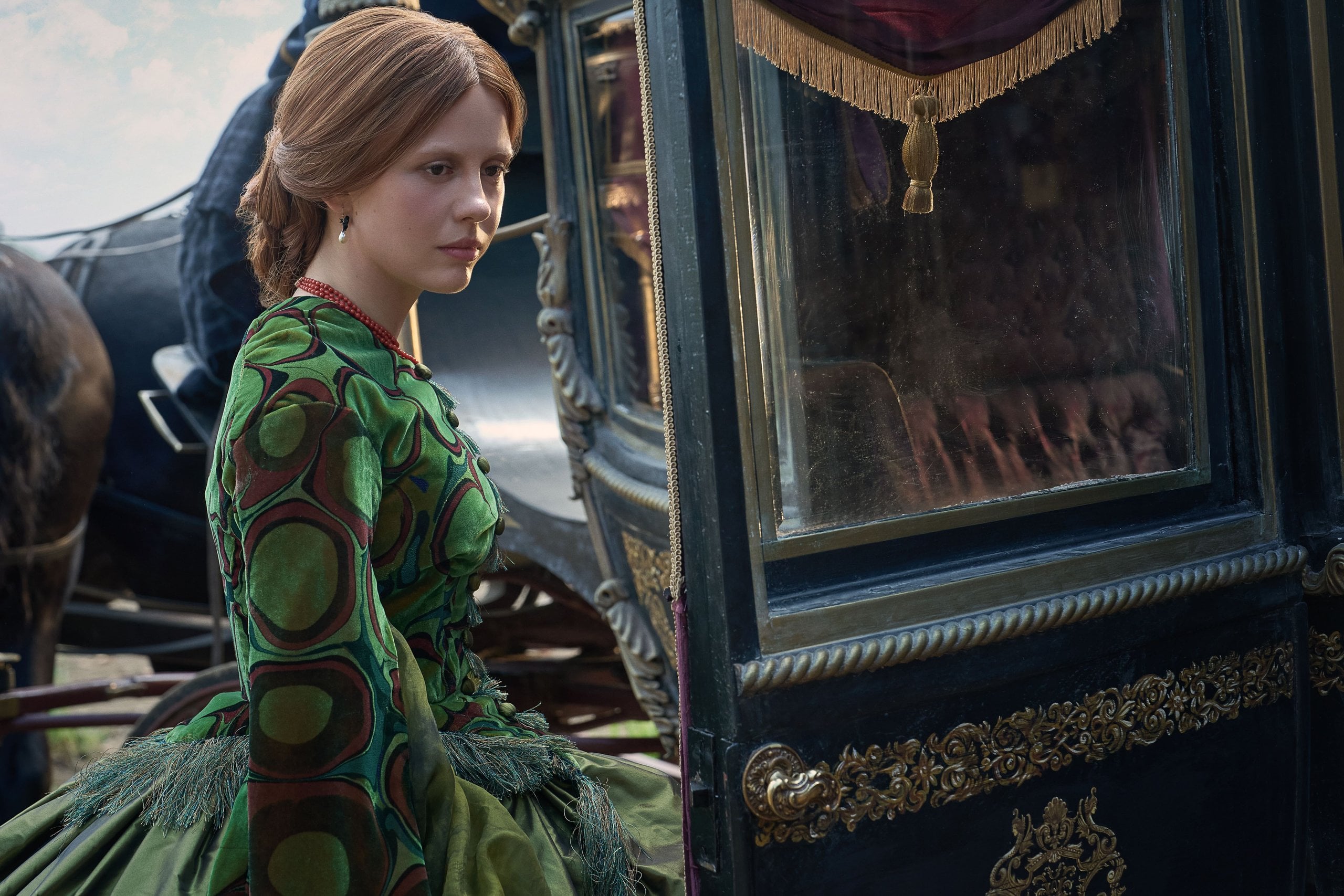 Mia Goth, in a green Victorian-era dress, steps into a horse-drawn carriage in a still from Frankenstein.