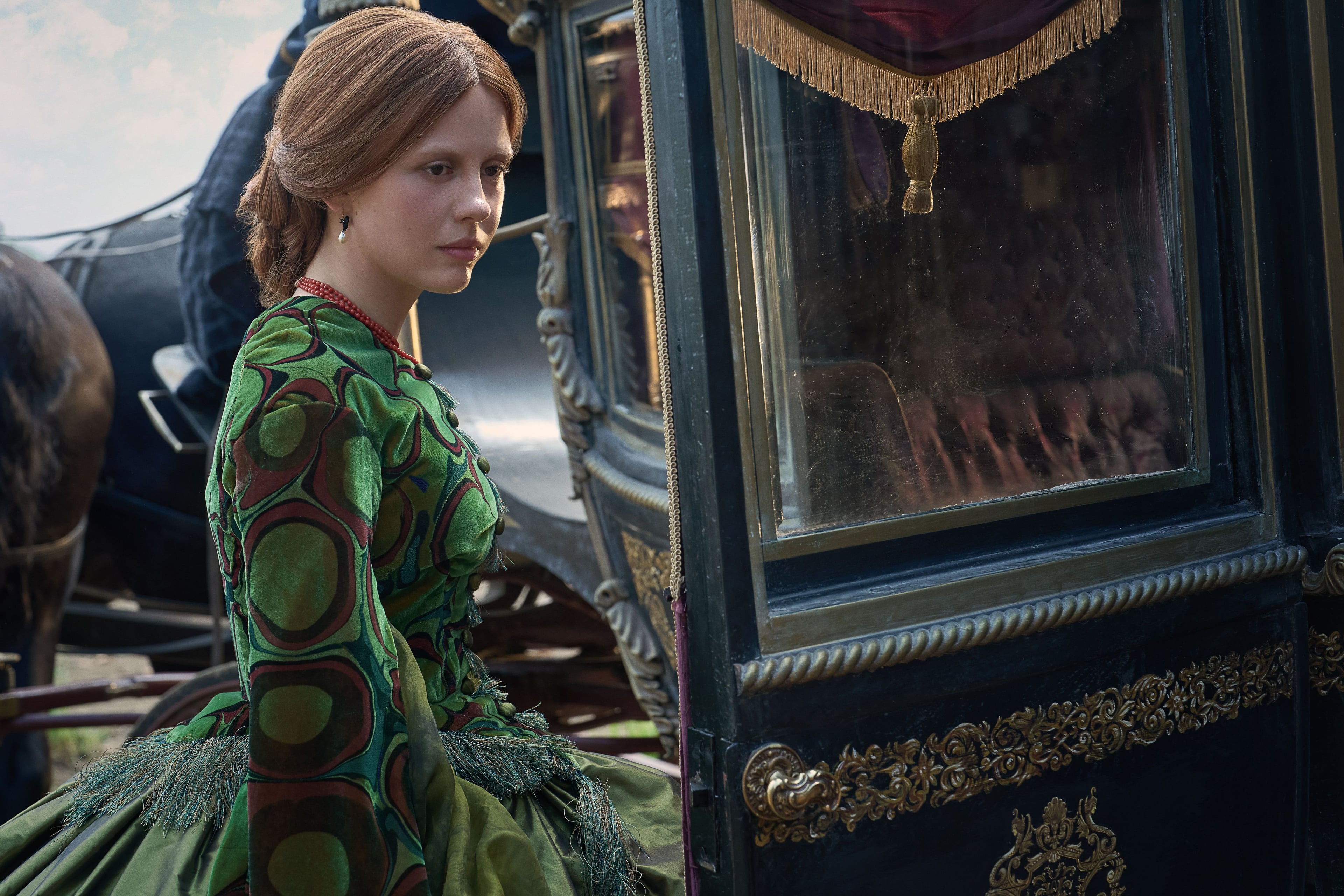 Mia Goth, in a green Victorian-era dress, steps into a horse-drawn carriage in a still from Frankenstein.