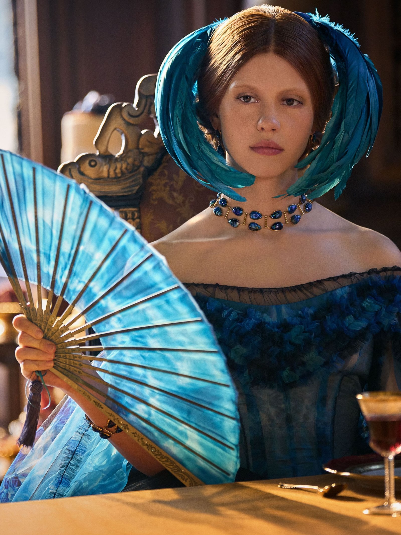 Mia Goth, in a turquoise-colored, Victorian-era dress, holds as matching fan, in a still from Frankenstein.