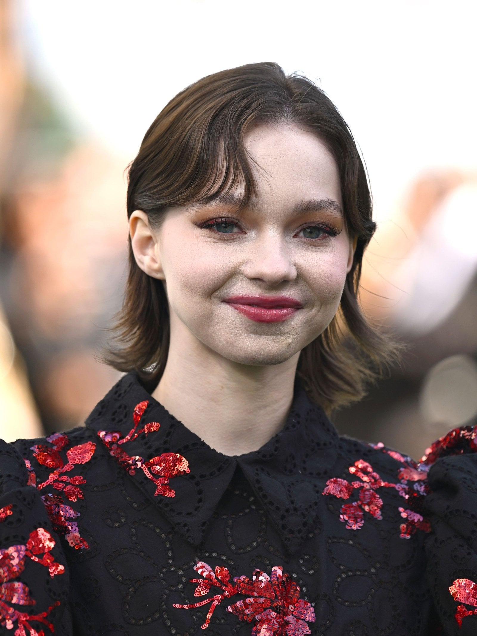 Emma Myers attends the World Premiere of "A Minecraft Movie" at the Cineworld Leicester Square on March 30, 2025 in London, England wearing pink lipstick and a black dress with pink flowers.