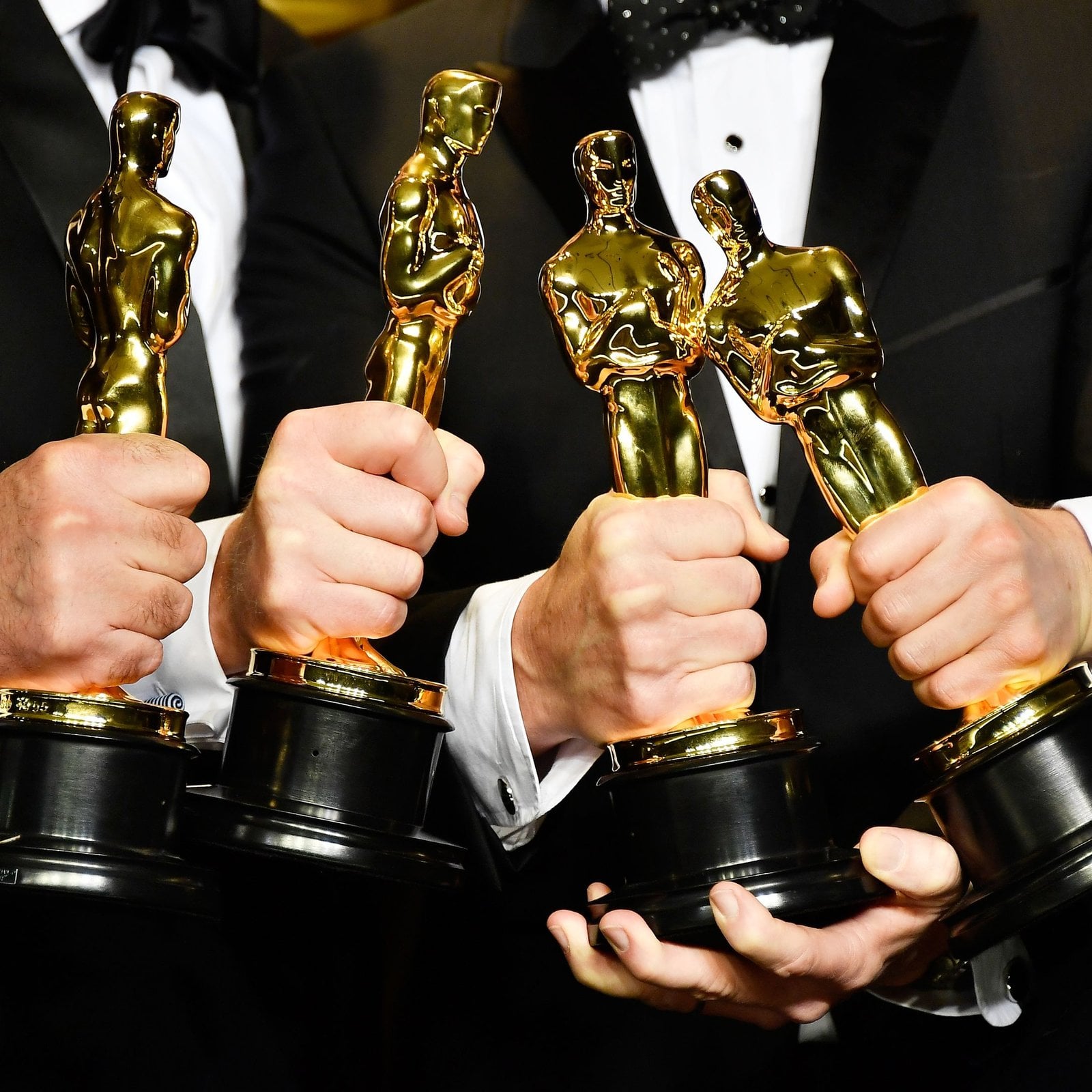 Hands holding four Oscar statuettes