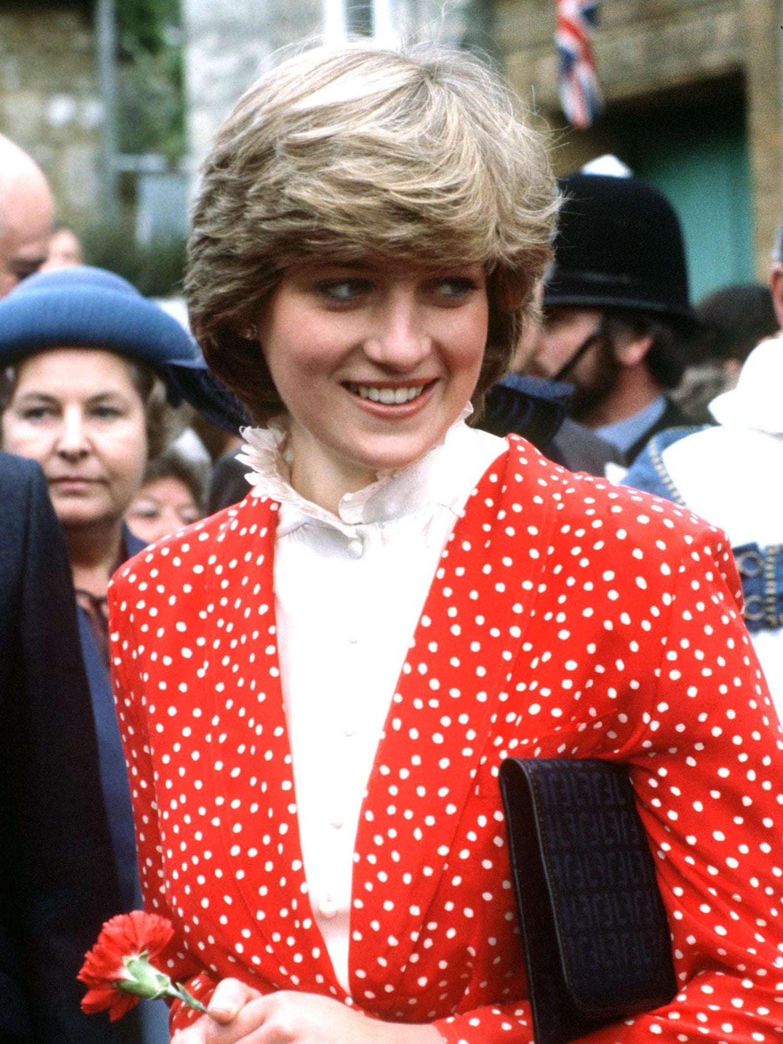 Princess Diana stands amongst a crowd on the street wearing a red-and-white polka dot dress in the 1980s.