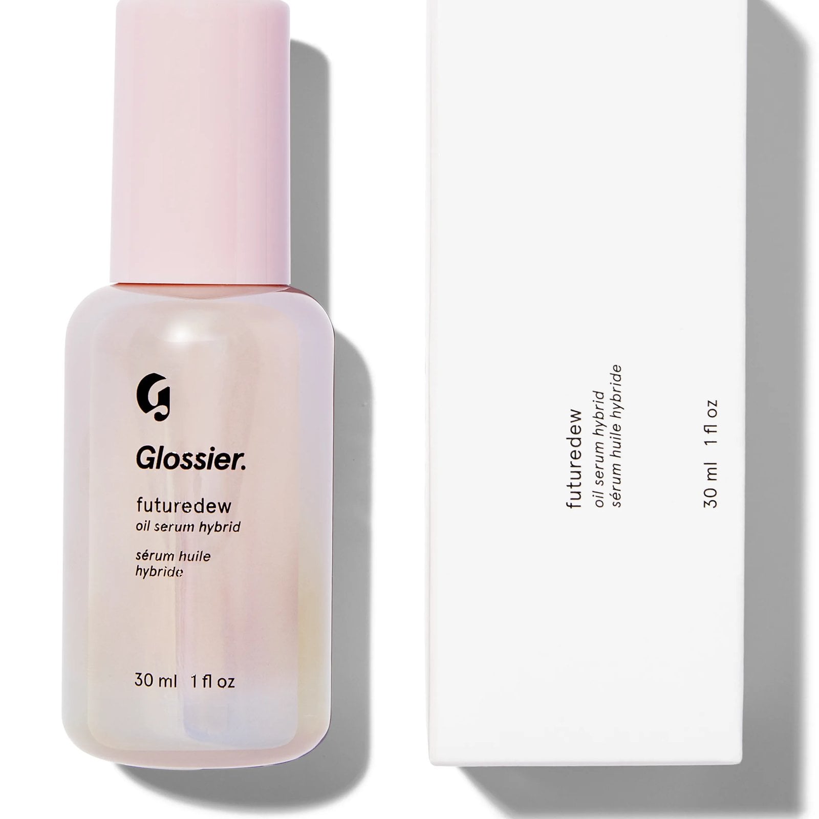 A light pink bottle of Glossier Future Dew next to a pale pink bottle and white box, on a white background