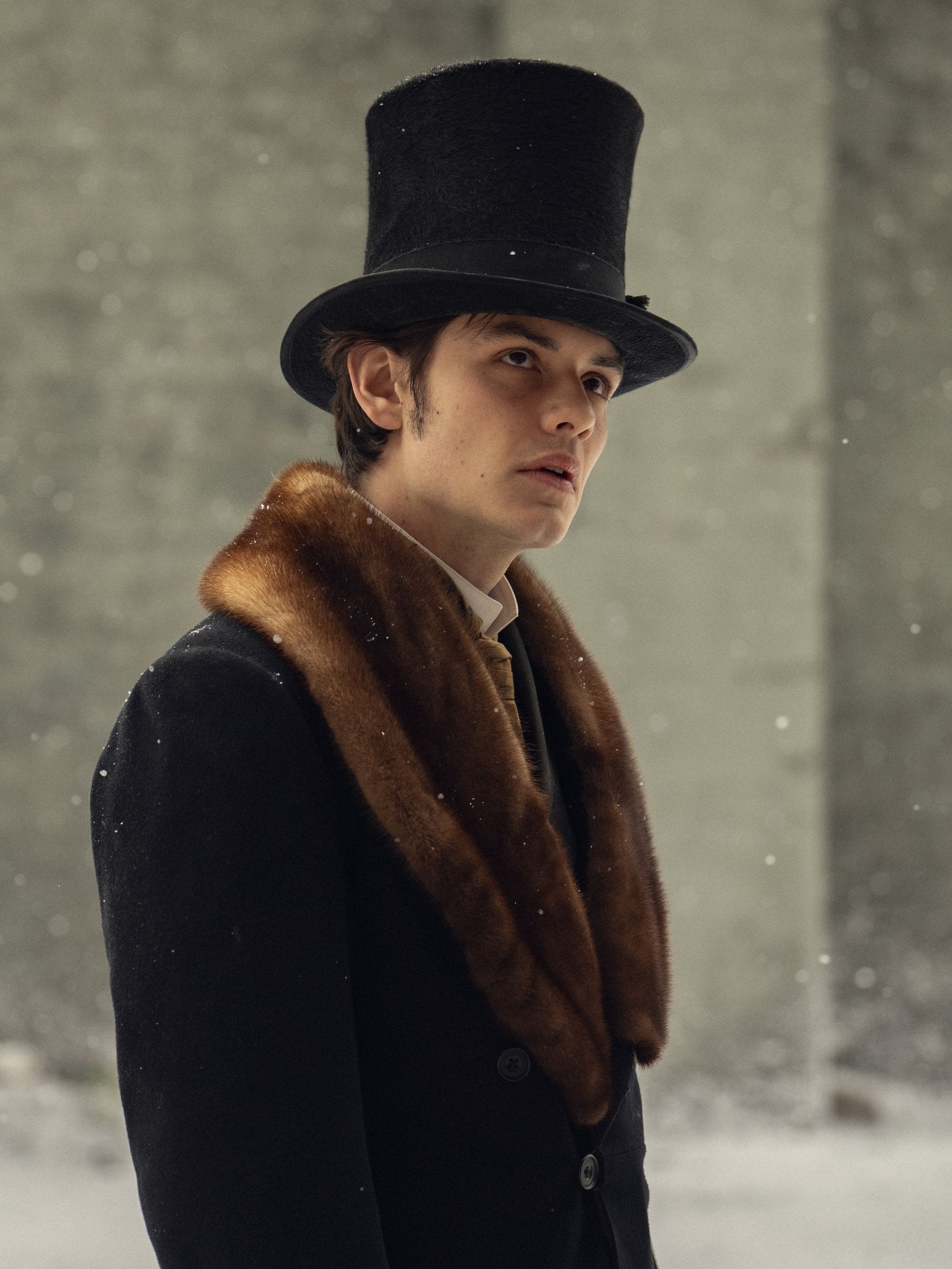 Actor Louis Partridge stands outside in the snow wearing a tall tophat and fur-lined coat in a still from the "House of Guinness."