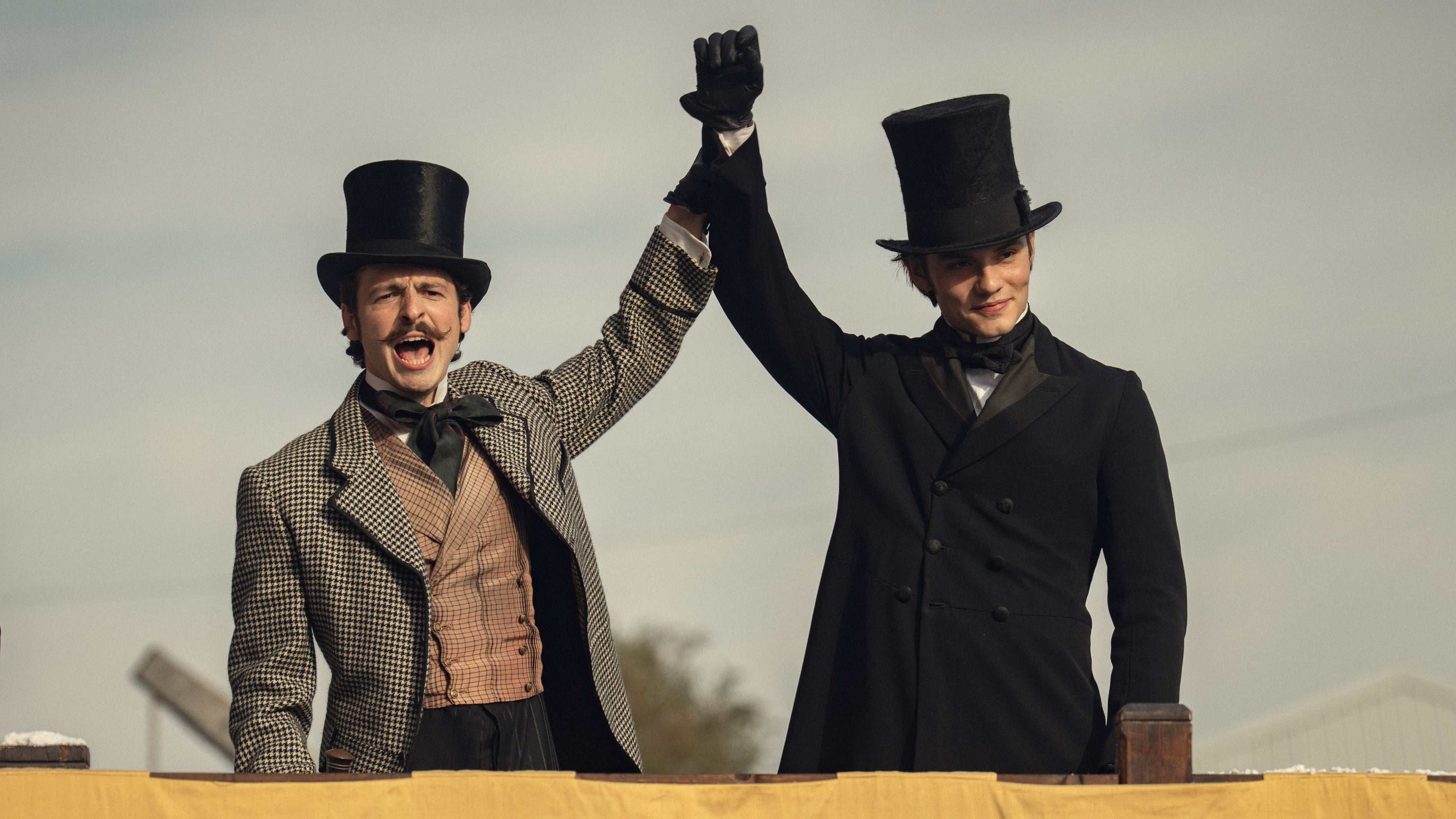 Actors Anthony Boyle and Louis Partridge hold eachother's hands in the air in a still from the "House of Guinness."