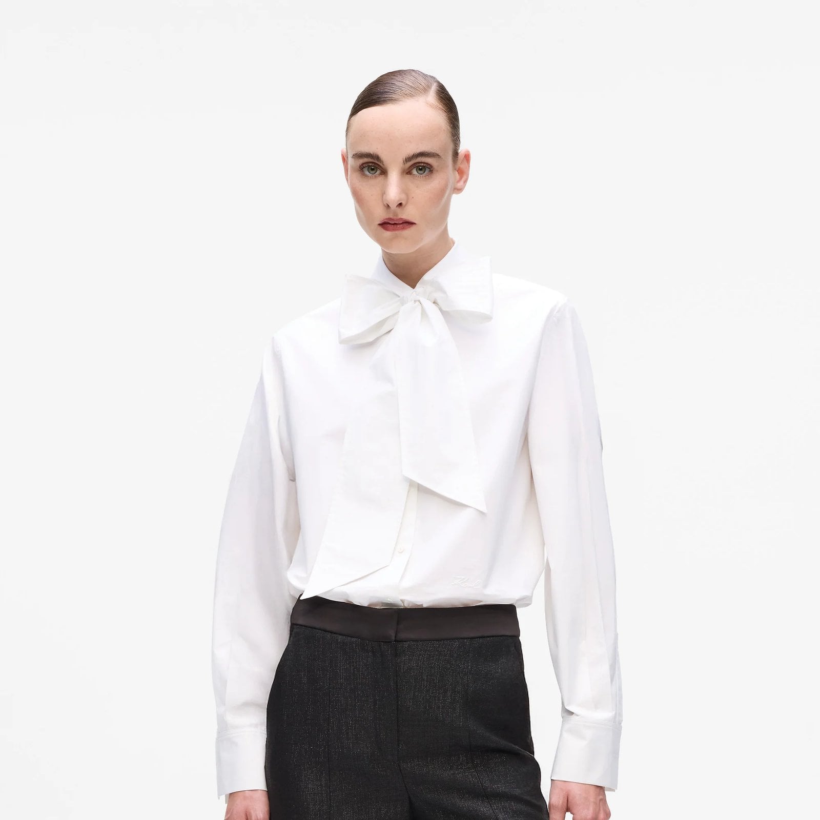 A model wears the Karl Lagerfeld Karl DNA Bow Detail Shirt and a pair of black trousers.