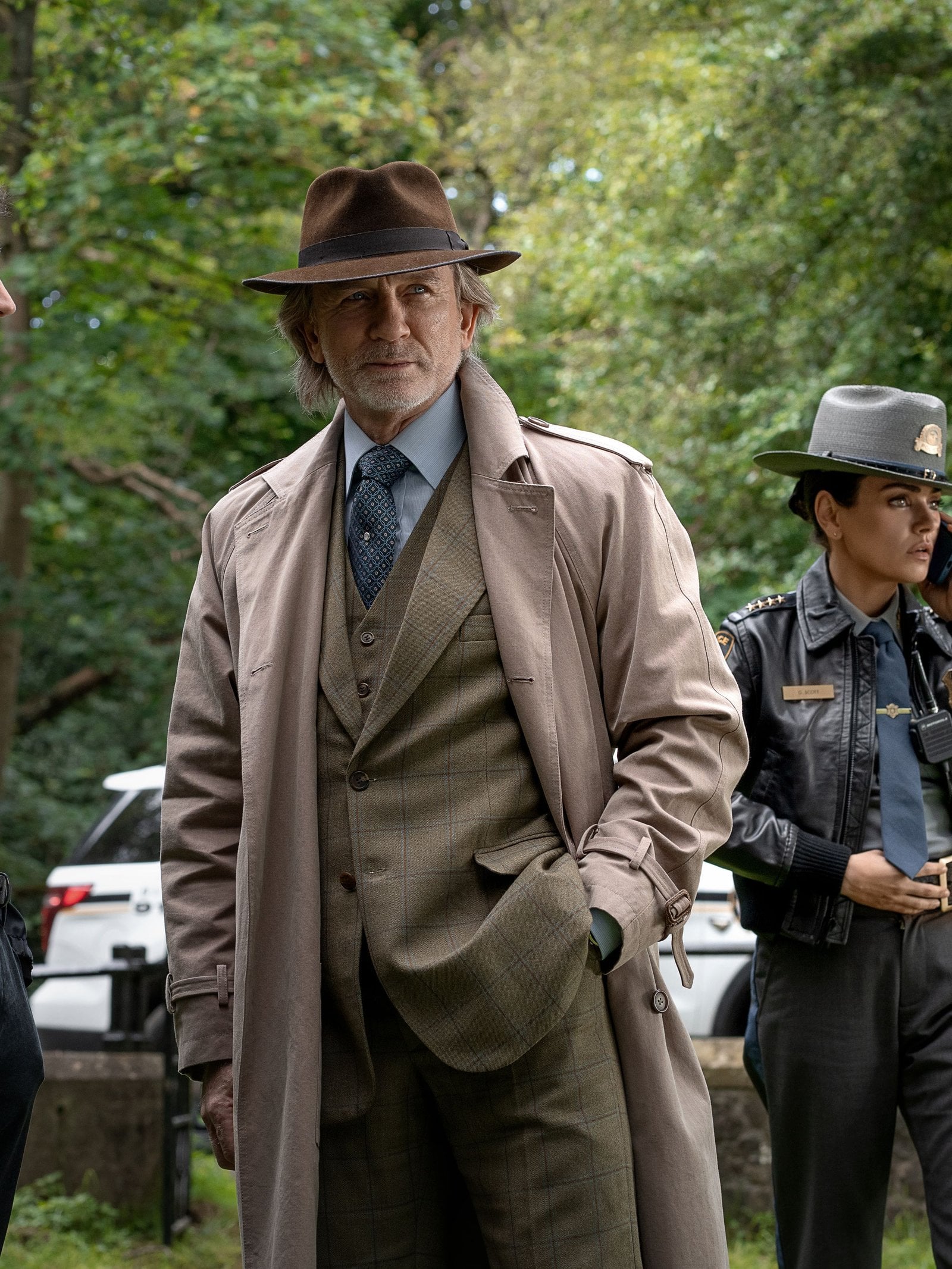 Actors Josh O'Connor, Daniel Craig,and Mila Kunis stand around outside in a still from "Wake Up Dead Man: A Knives Out Mystery."