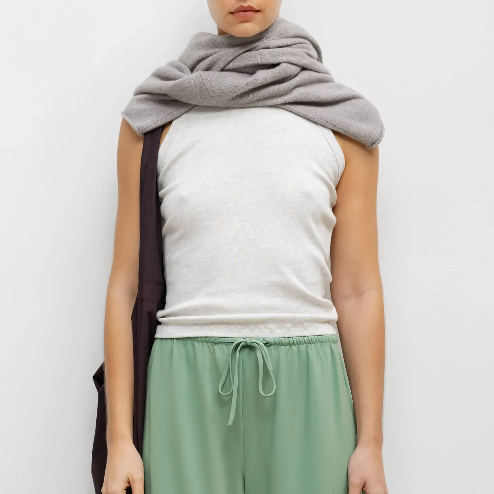 a woman wearing a white tank top with green pants and a sweater wrapped around her neck