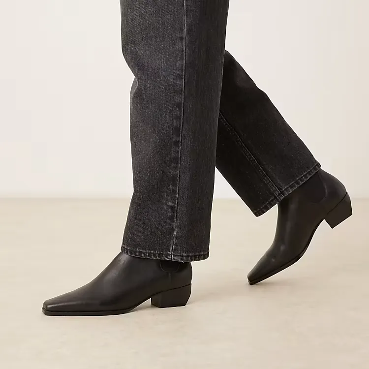 The bottom half of a model's legs, wearing the Mango leather square toe low heel ankle boots in black.