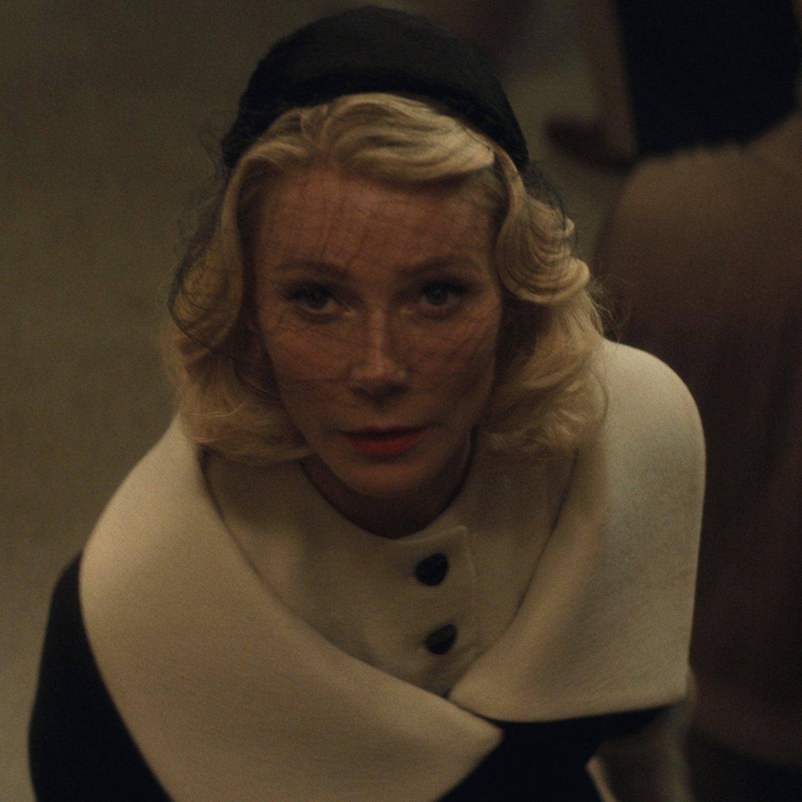Gwyneth Paltrow in 50s-stule clothing, looking up at the camera in a scene from Marty Supreme.