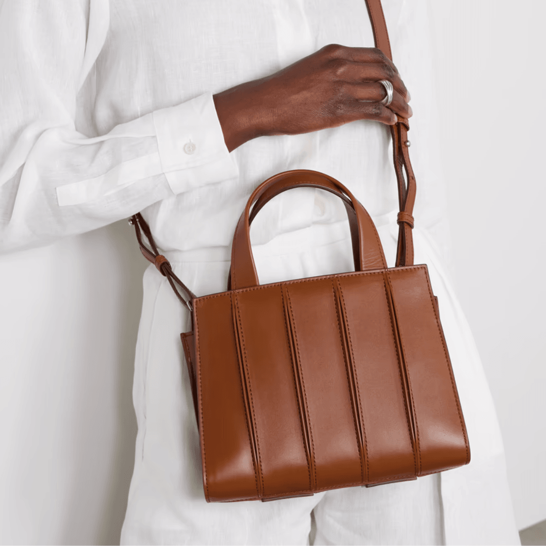 A model in all white wears a brown Max Mara Whitney Bag 4 small pleated leather tote