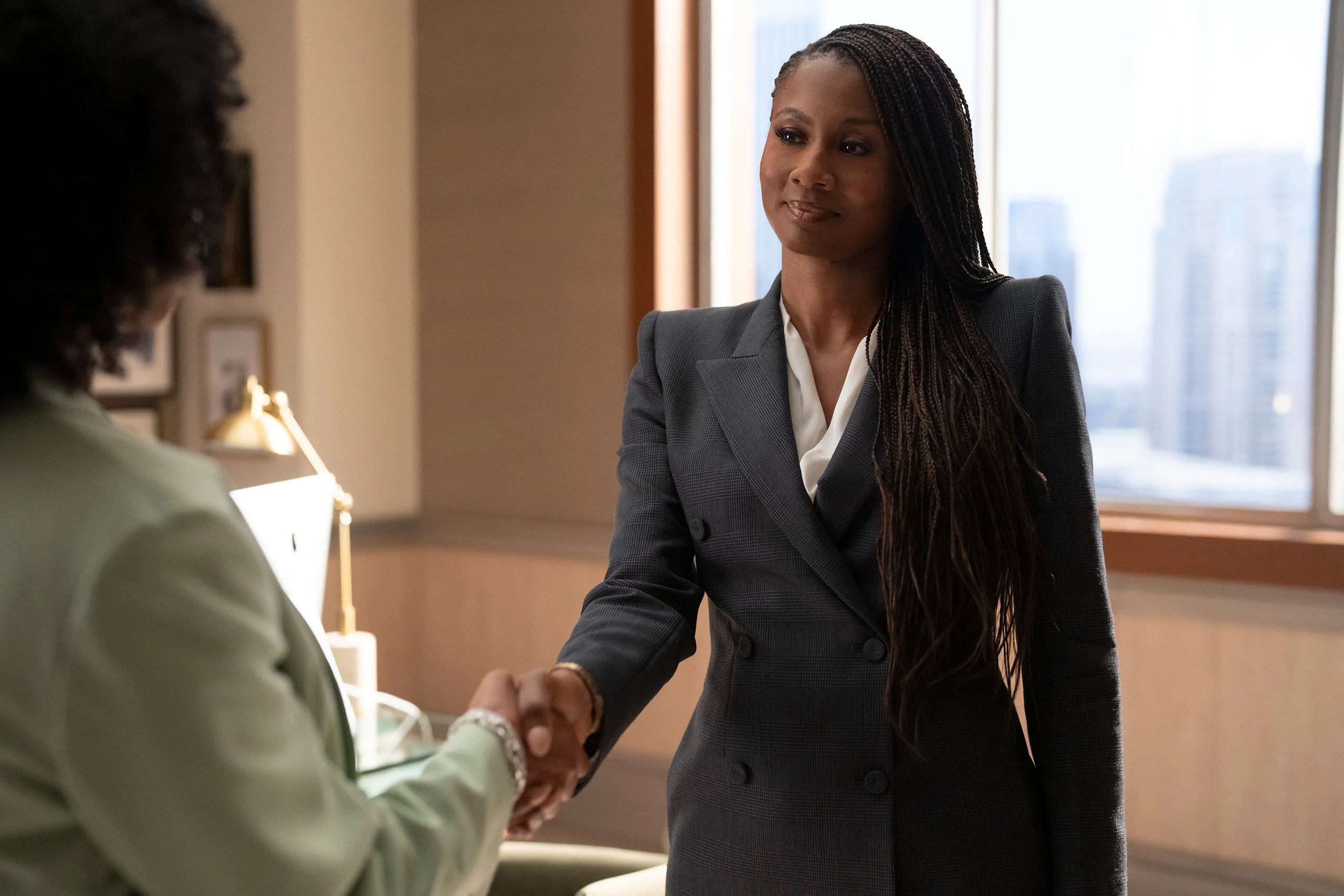 Actress Emayatzy Corinealdi shakes someone's hand in a gray suit in a still from "Reasonable Doubt."