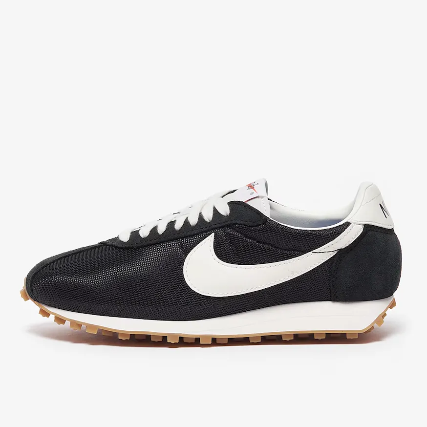 A pair of black Nike shoes with the white swoosh logo against an off-white background