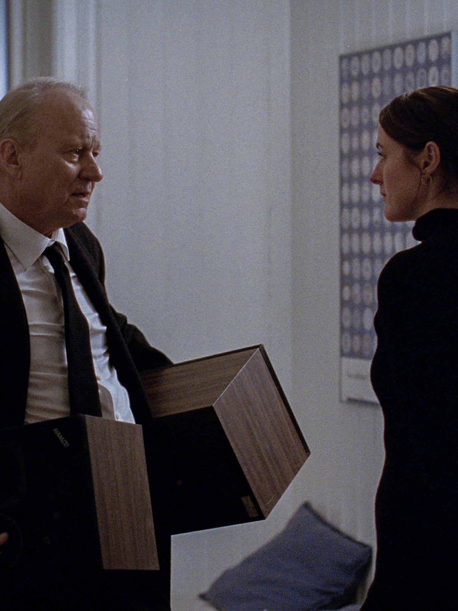 Stellan Skarsgård holding two boxes next to Renate Reinsve in "Sentimental Value."