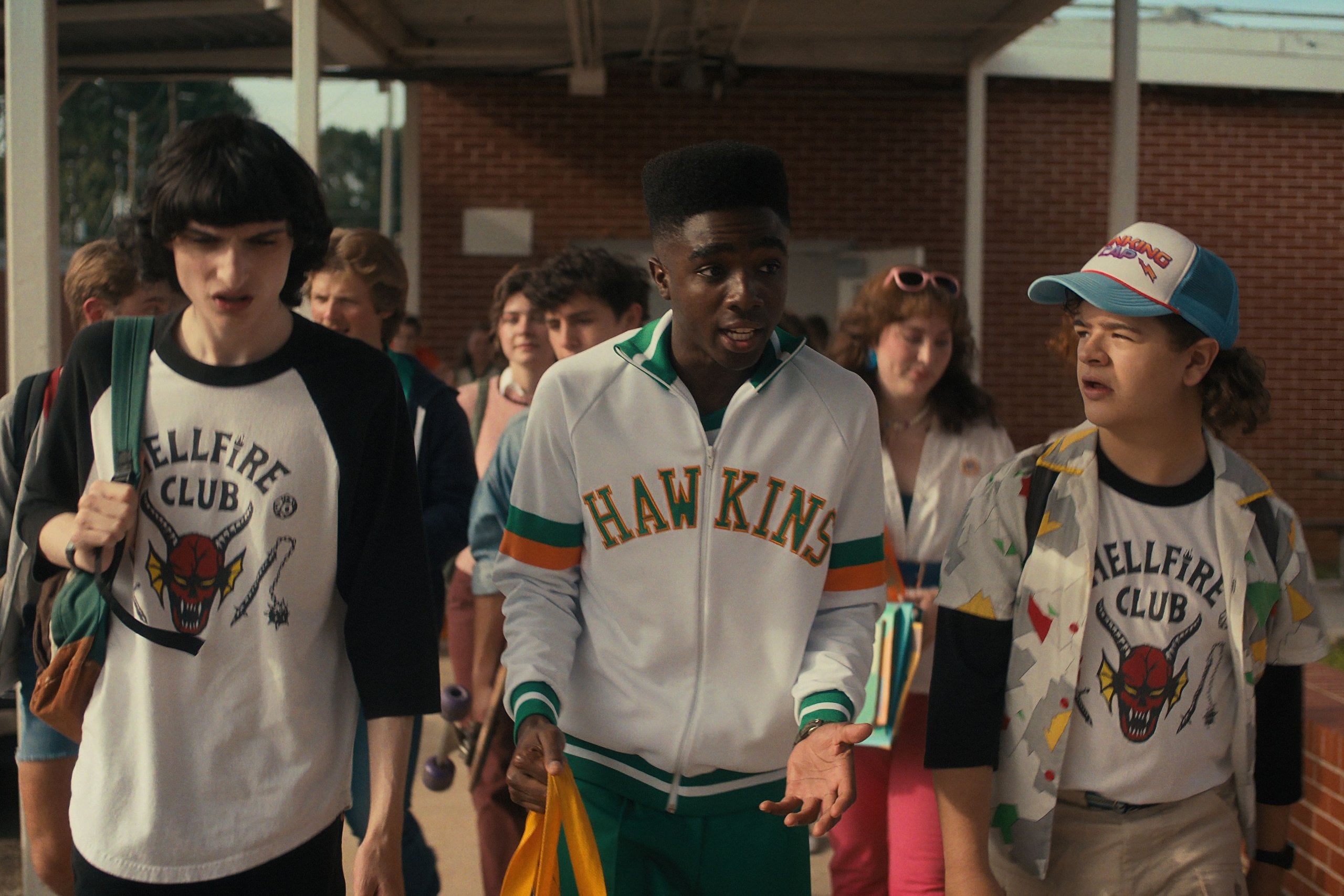 Actors Finn Wolfard, Caleb McLaughlin, and Gaten Matarazzo exiting high school in a still from Stranger Things.