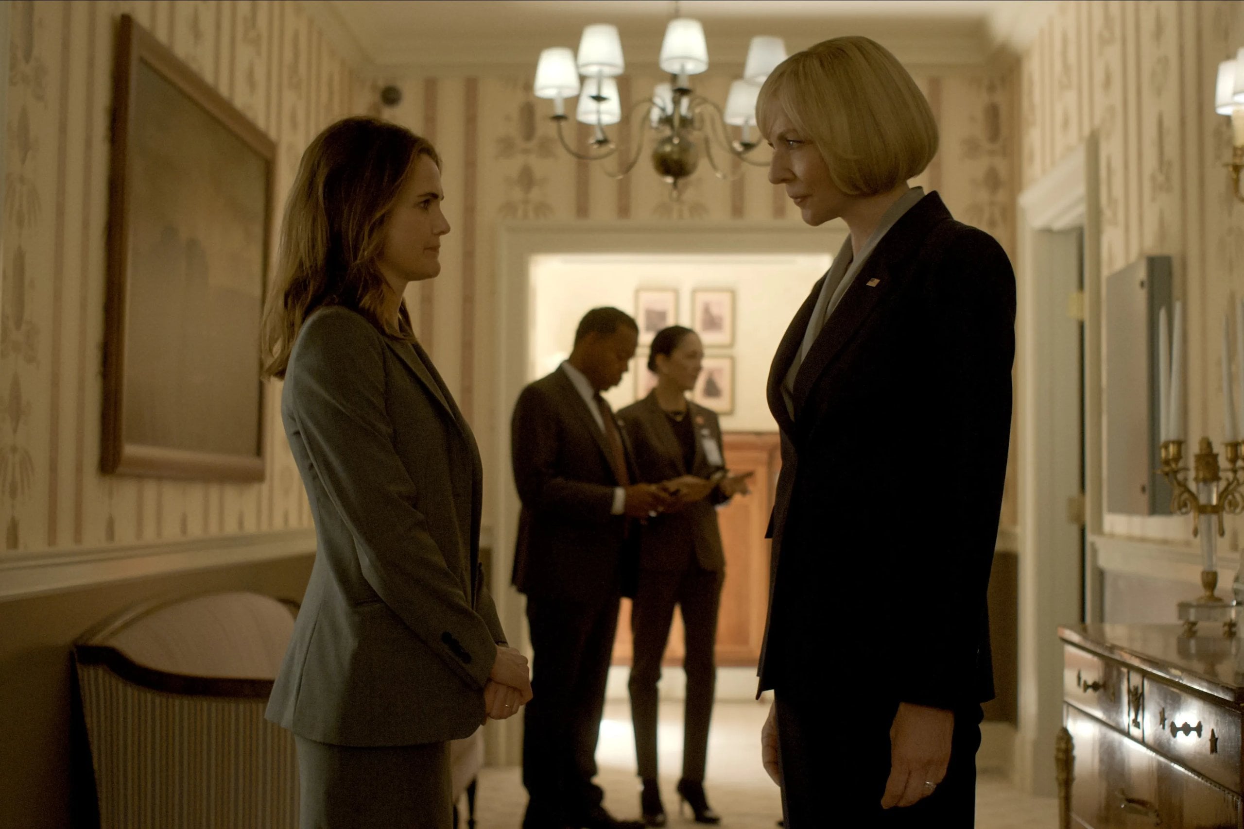Actors Keri Russell and Allison Janney stand in a grand hallway looking at each other in a still from The Diplomat.
