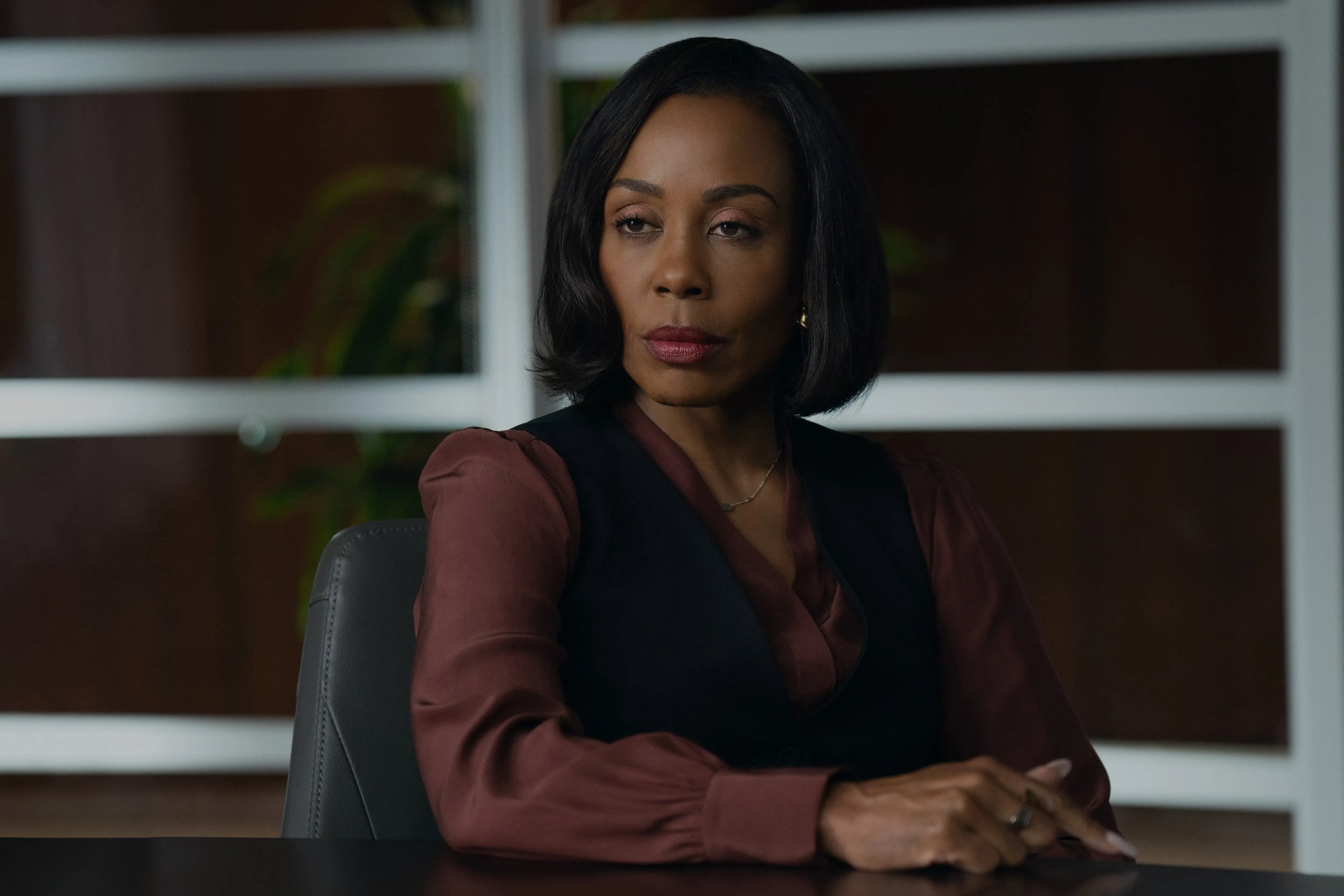 Karen Pittman sits at a desk in a brown silk top and black vest a still from The Morning Show.