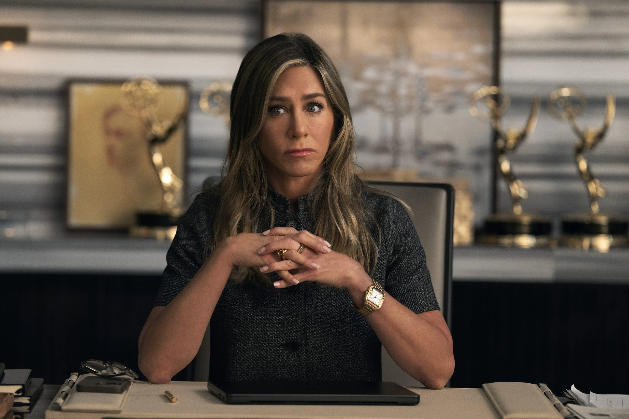 Jennifer Aniston sits at a desk with her fingers interlaced in a still from "The Morning Show." .