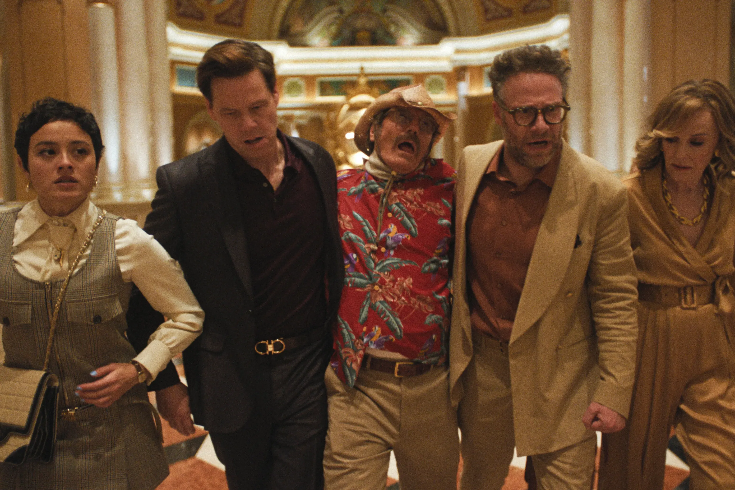 The cast of the studio walking in a line, looking worried and holding up actor Bryan Cranston.