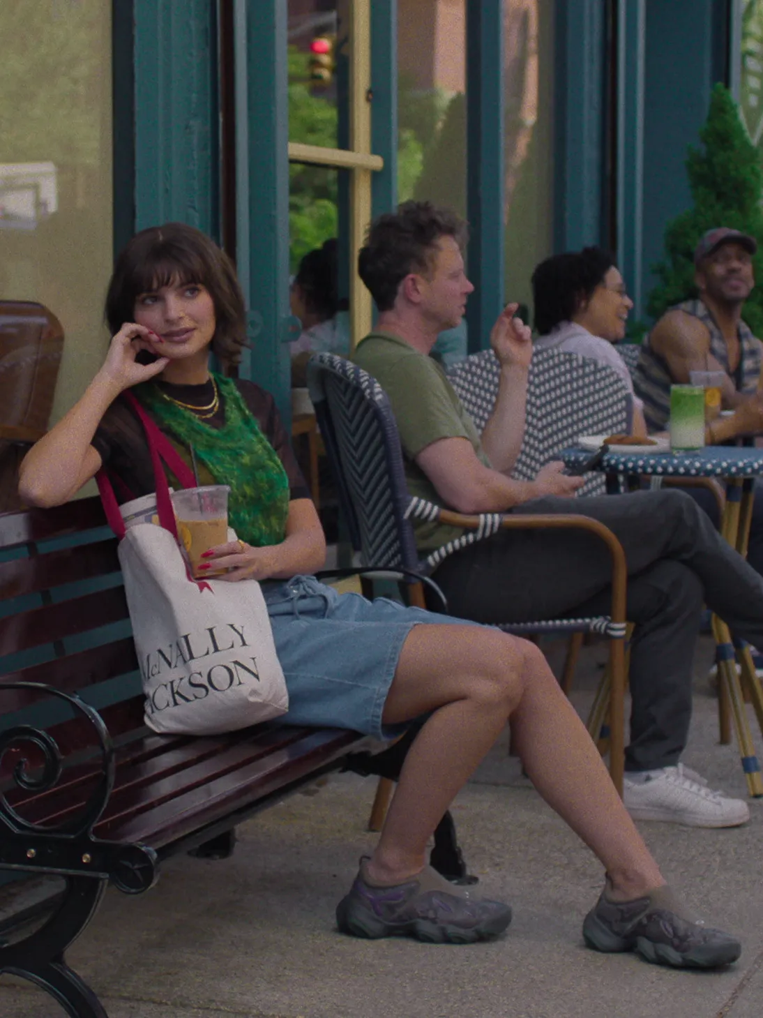 Actress Emily Ratajkowski sits on a bench outside a cafe, talking on the phone.